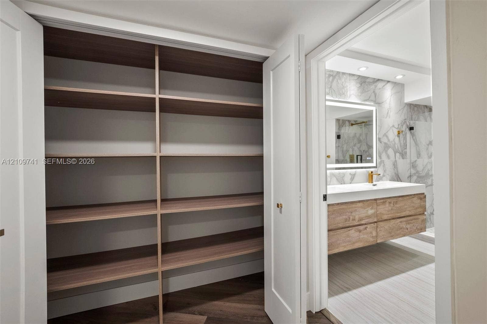 19101 NE 36th Court, #203, Aventura, FL 33180 Built-in storage closet featuring wood-finish shelving, and bathroom with a floating wood-finish vanity, integrated rectangular sink, wall-mounted faucet, and stone-finish wall tile