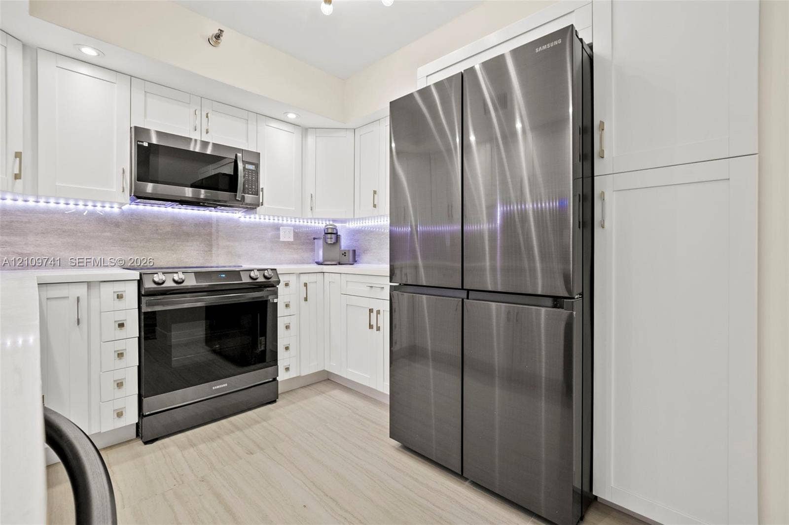 19101 NE 36th Court, #203, Aventura, FL 33180 Kitchen featuring white shaker-style cabinetry, stainless steel appliances, stone-surface countertops, under-cabinet lighting, and wood-finish flooring