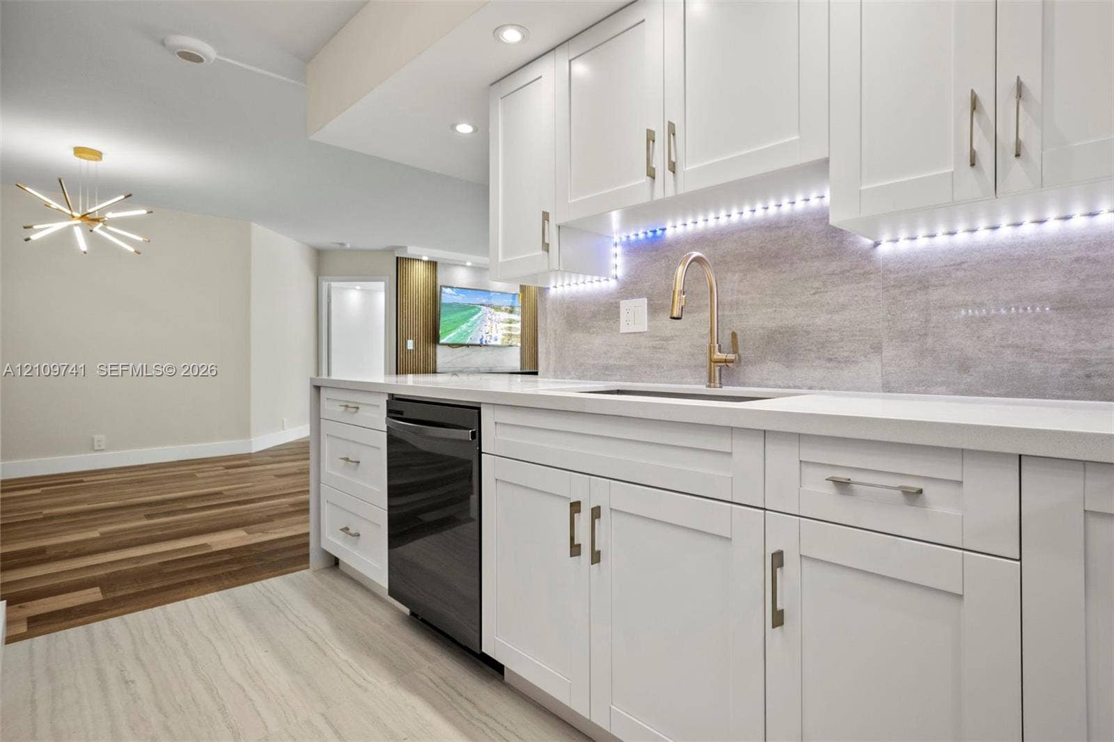19101 NE 36th Court, #203, Aventura, FL 33180 White Shaker-style cabinetry, matte stone-finish backsplash, undermount sink with high-arc faucet, integrated under-cabinet lighting, and wood-finish flooring