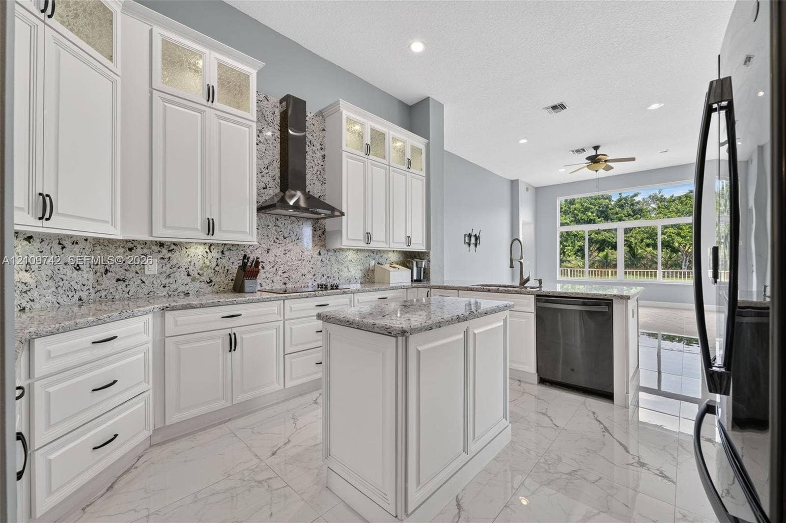 19143 SW 60th Court, Pembroke Pines, FL 33332 Kitchen featuring white cabinetry with glass-panel upper doors, stone-finish countertops, full-height decorative backsplash, stainless steel range hood, and large-format tile flooring