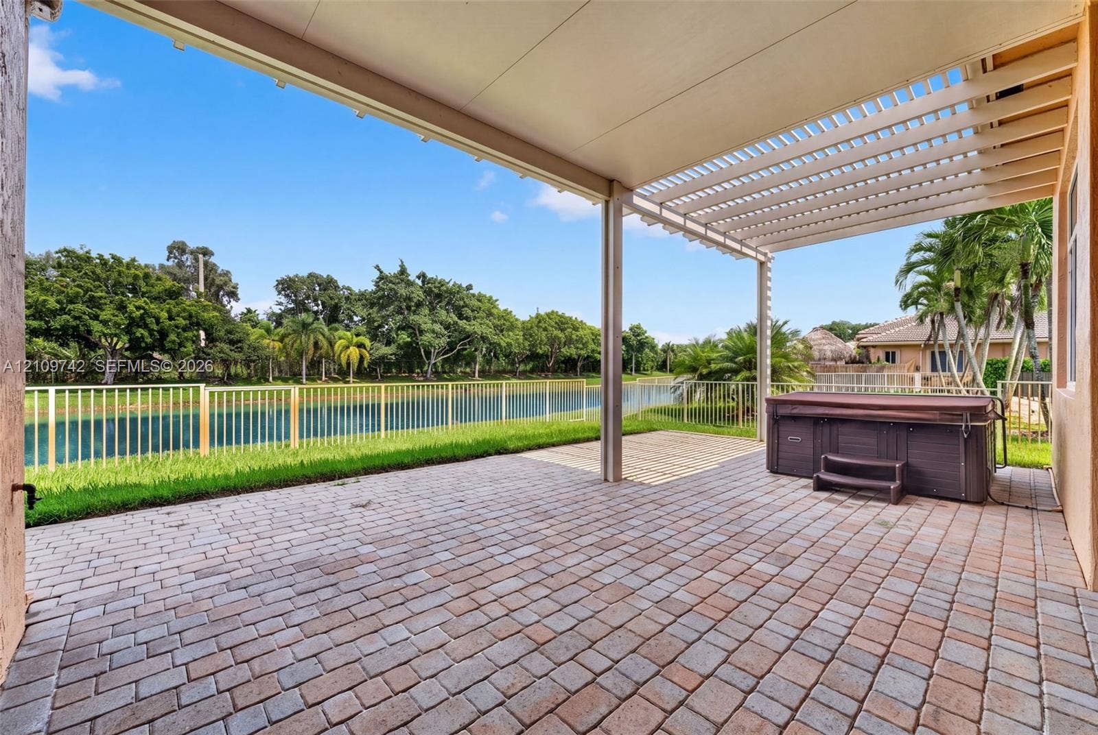19143 SW 60th Court, Pembroke Pines, FL 33332 Covered paver patio featuring an attached pergola, built-in spa, and metal perimeter fencing overlooking the water