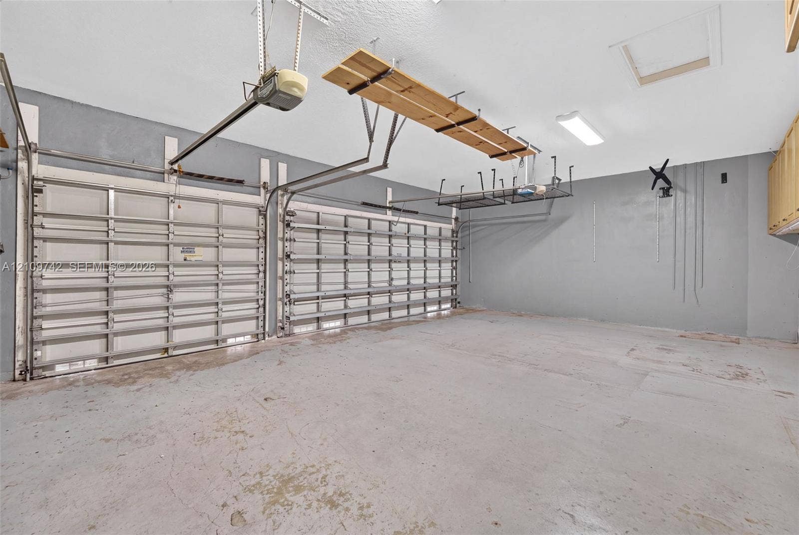 19143 SW 60th Court, Pembroke Pines, FL 33332 Two-car garage featuring dual overhead metal doors, painted concrete flooring, ceiling-mounted storage racks, and built-in wall cabinetry