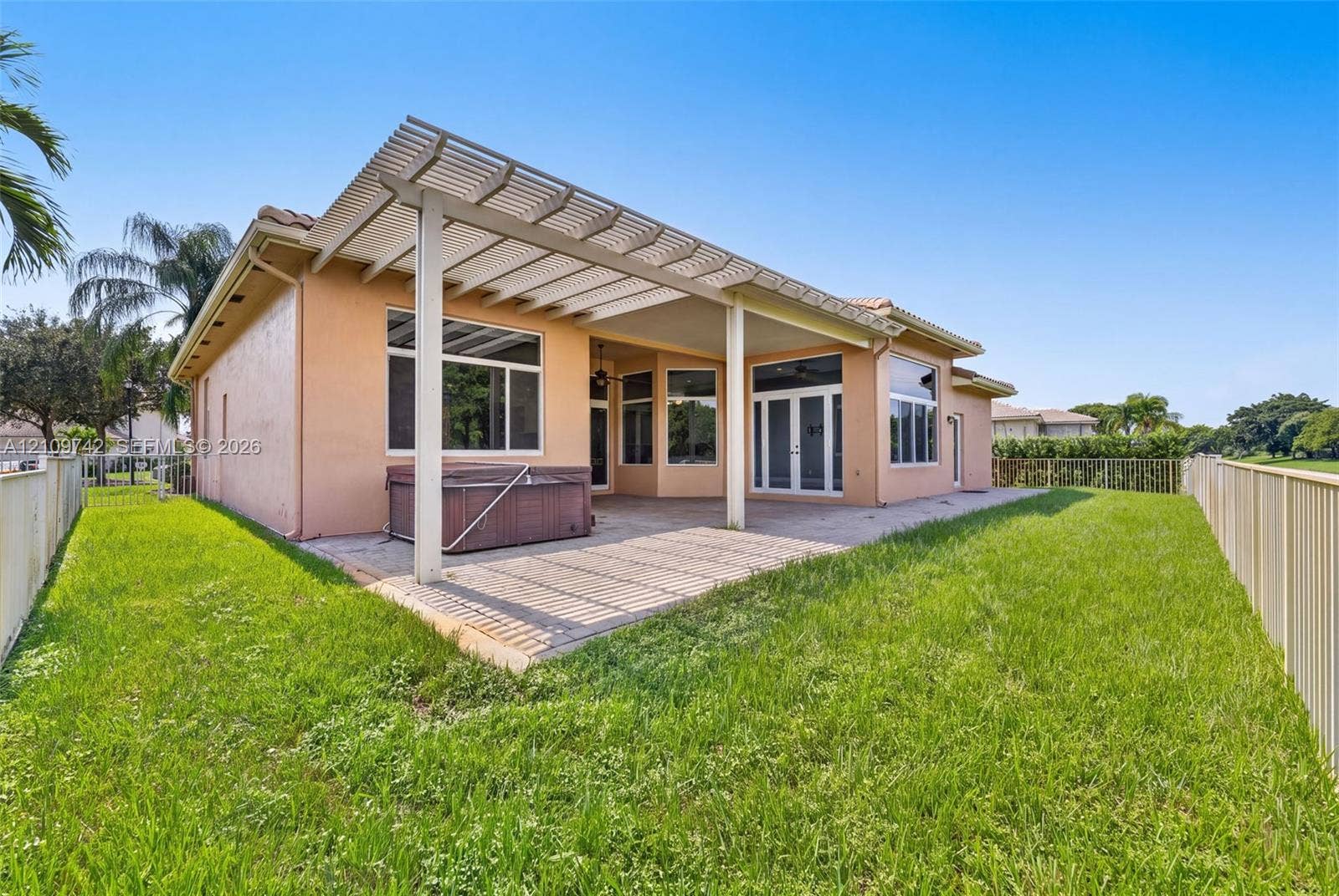 19143 SW 60th Court, Pembroke Pines, FL 33332 Stucco exterior featuring a covered patio, trellis-style roof extension, concrete hardscaping, and surrounding metal fencing