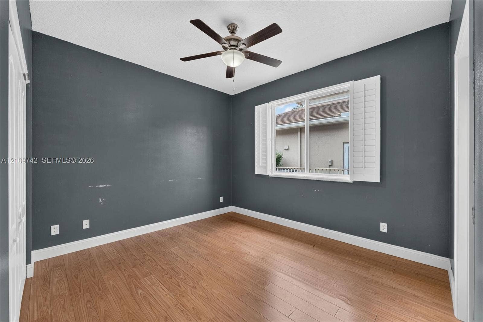 19143 SW 60th Court, Pembroke Pines, FL 33332 Interior room featuring wood-finish flooring, dark-toned walls, a five-blade ceiling fan with integrated lighting, and plantation-style window shutters