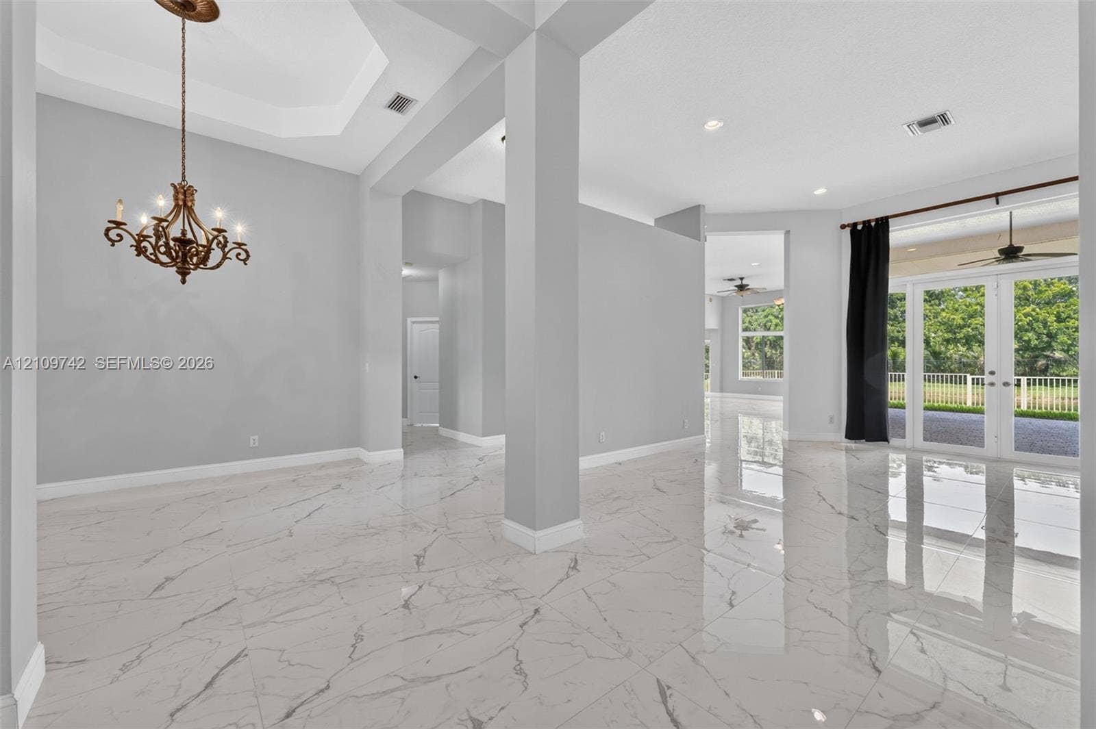 19143 SW 60th Court, Pembroke Pines, FL 33332 Interior featuring polished stone-finish tile flooring, a tray ceiling, an ornate metal chandelier, architectural support columns, and French doors