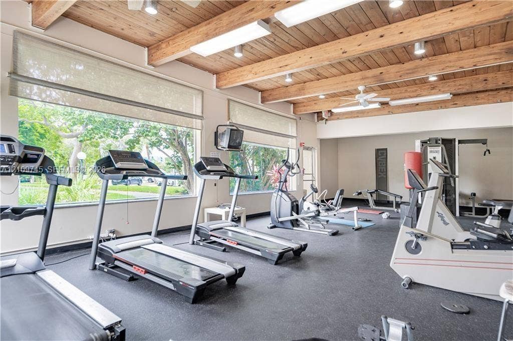 Fitness center featuring exposed wood ceiling beams, expansive windows, rubberized flooring, and integrated ceiling lighting
