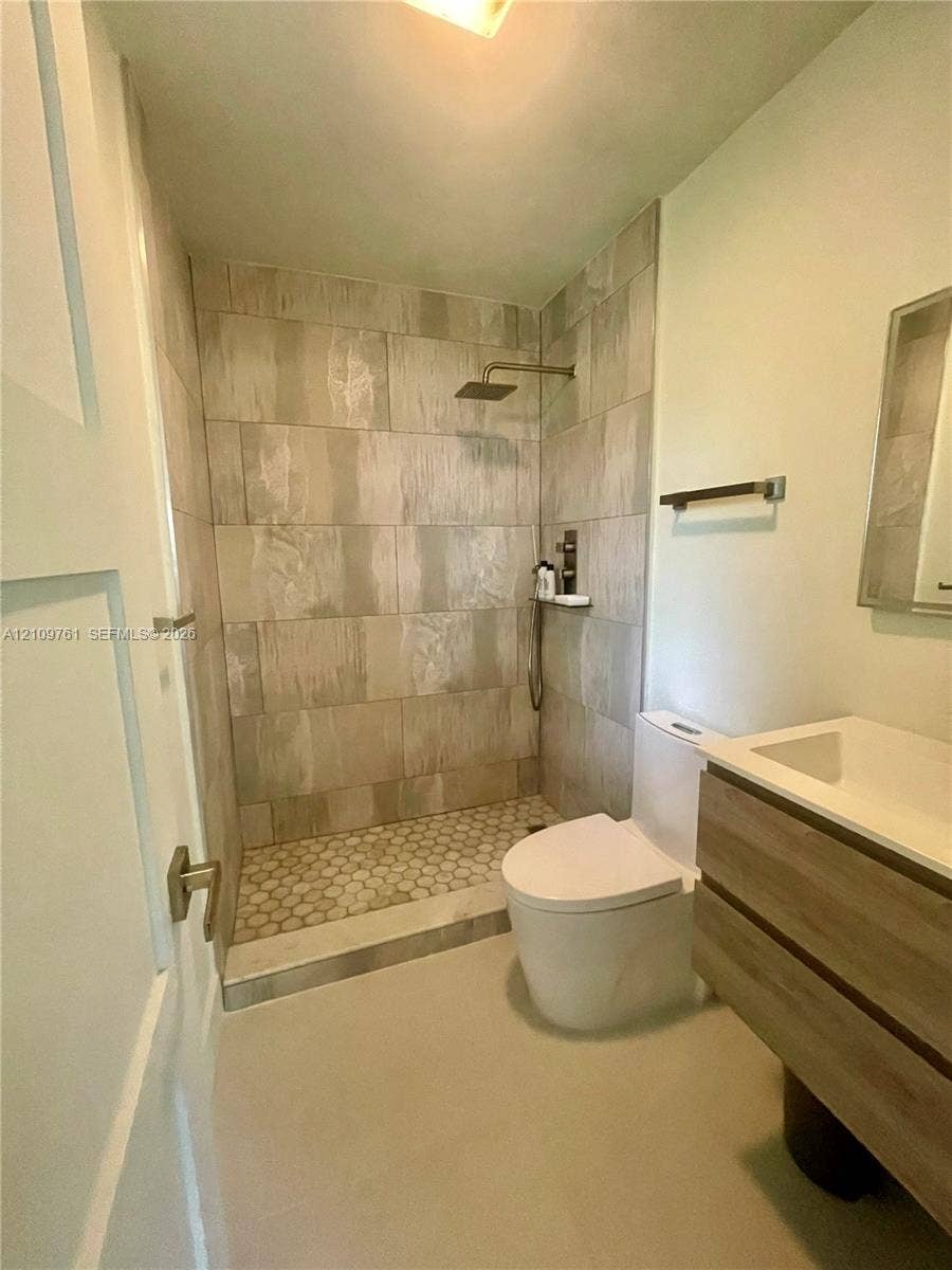 Walk-in shower featuring large-format wall tile, hexagonal floor tile, and a rainfall showerhead, paired with a floating wood-finish vanity and integrated rectangular sink