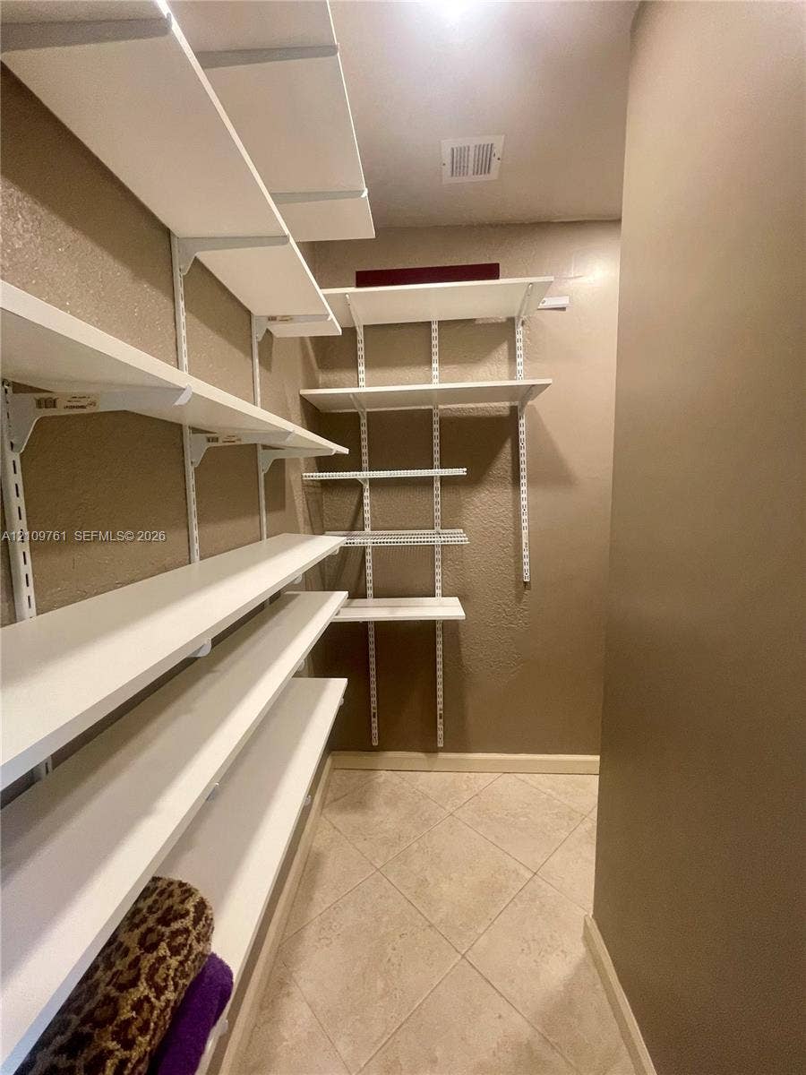 Storage area featuring white adjustable shelving units, tile flooring, and neutral wall paint