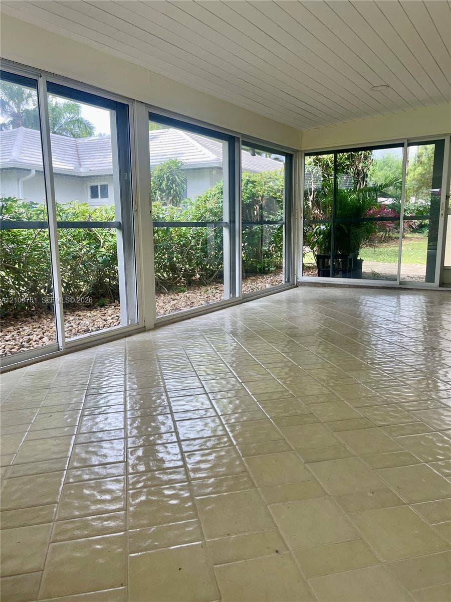 Enclosed sunroom featuring light-colored ceramic tile flooring, beadboard ceiling, and multiple floor-to-ceiling sliding glass doors