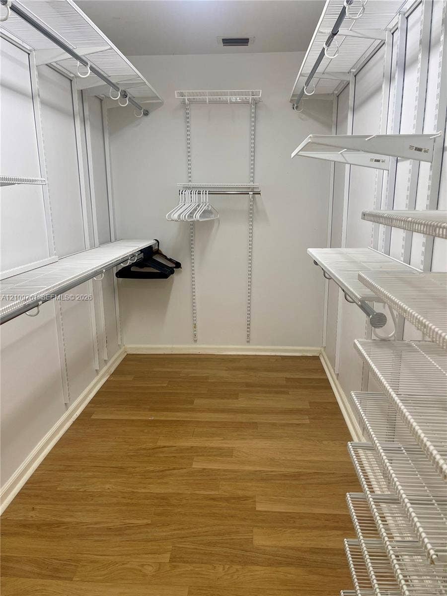 Walk-in closet featuring wood-finish flooring and integrated white wire shelving systems with multiple hanging rods and tiered storage racks