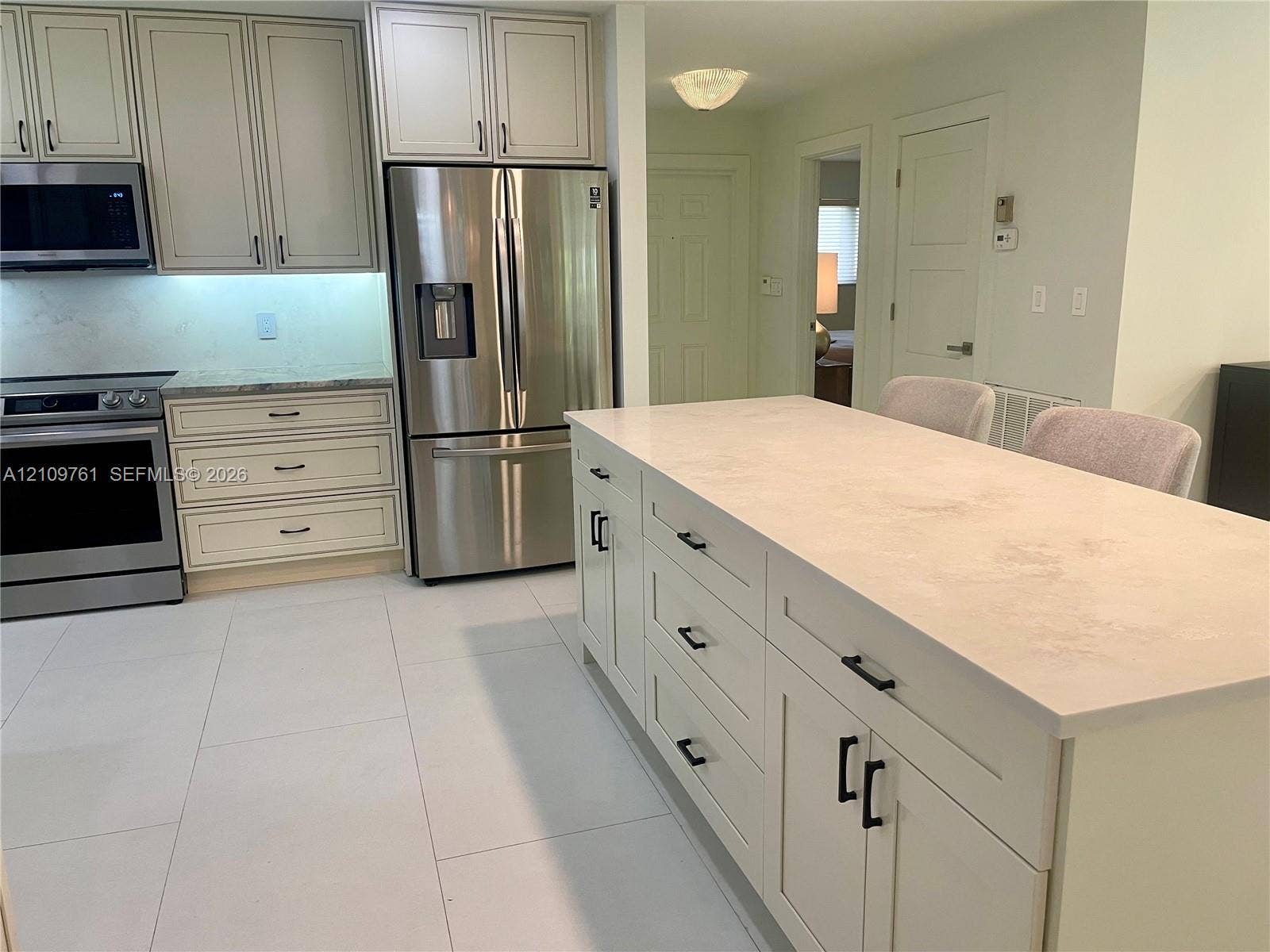 Kitchen featuring an expansive central island with stone-finish countertops, stainless steel appliances, shaker-style cabinetry, and large-format tile flooring