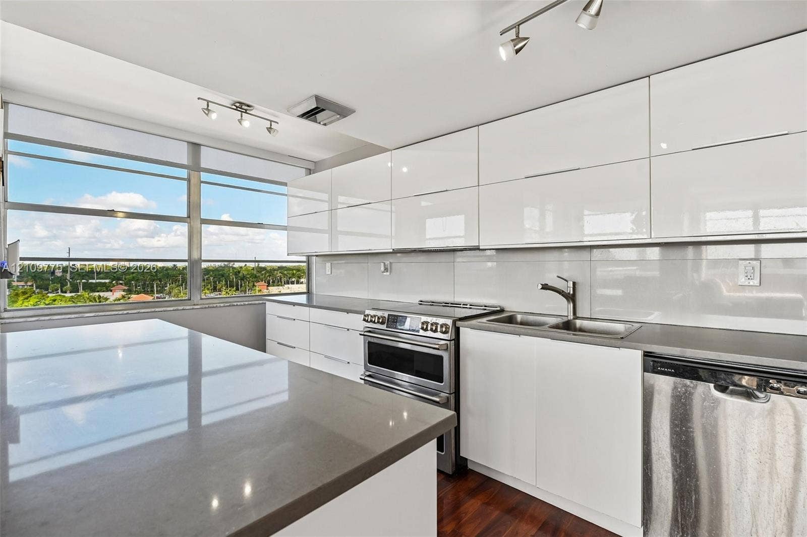 Kitchen featuring glossy white flat-panel cabinetry, a stainless steel range, a solid-surface island countertop, and wood-finish flooring, complemented by a large horizontal window