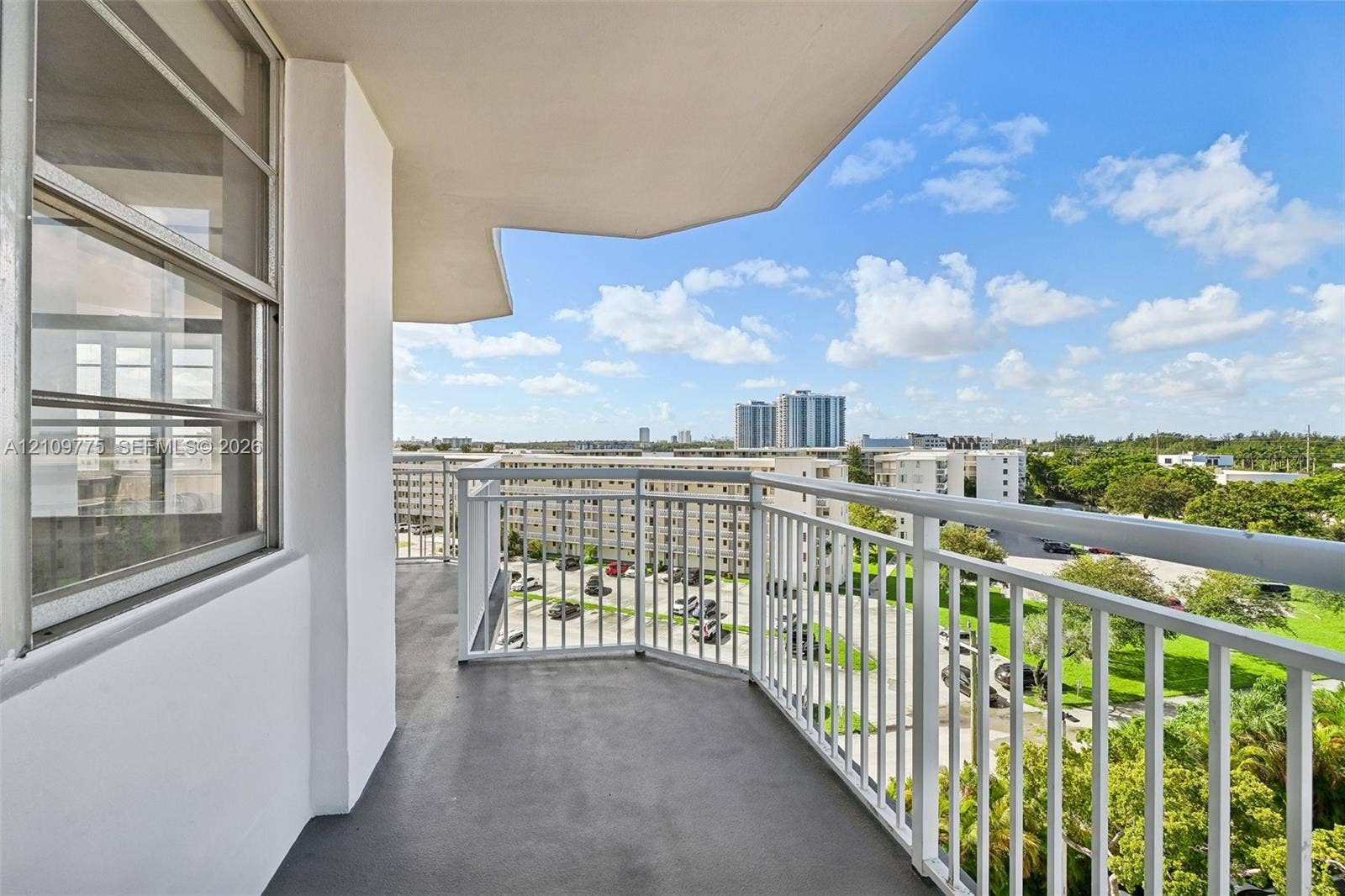 Covered balcony featuring white metal railings, concrete flooring, and sliding glass entry doors