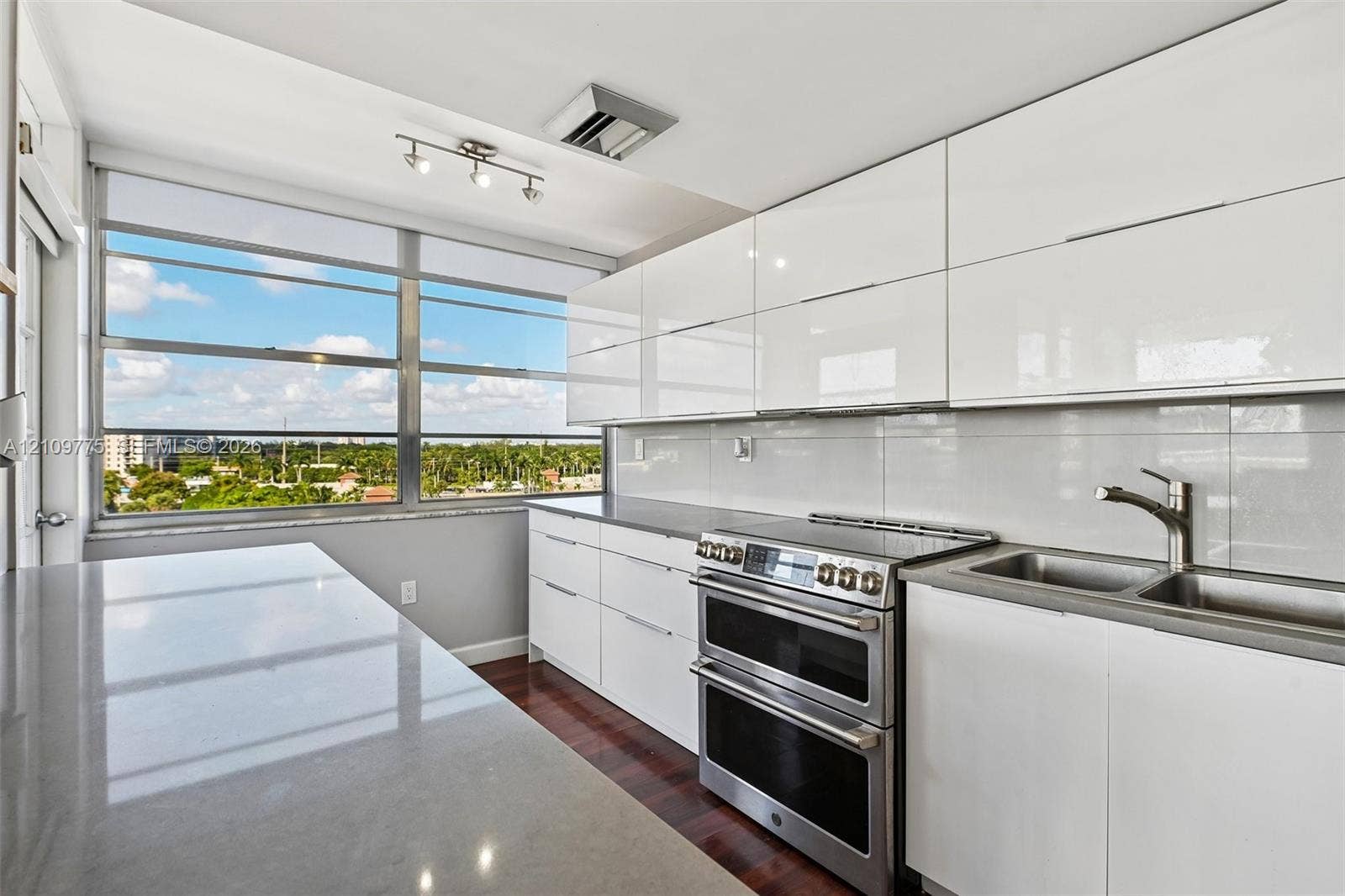 High-gloss white cabinetry, expansive stone countertops, stainless steel dual-oven range, double basin undermount sink, and floor-to-ceiling windows