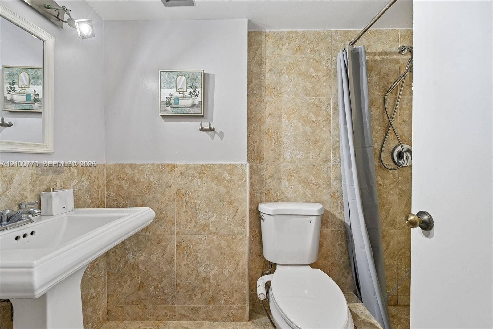 Pedestal sink with chrome faucet, wall-mounted vanity mirror, and floor-to-ceiling neutral-toned tile shower enclosure
