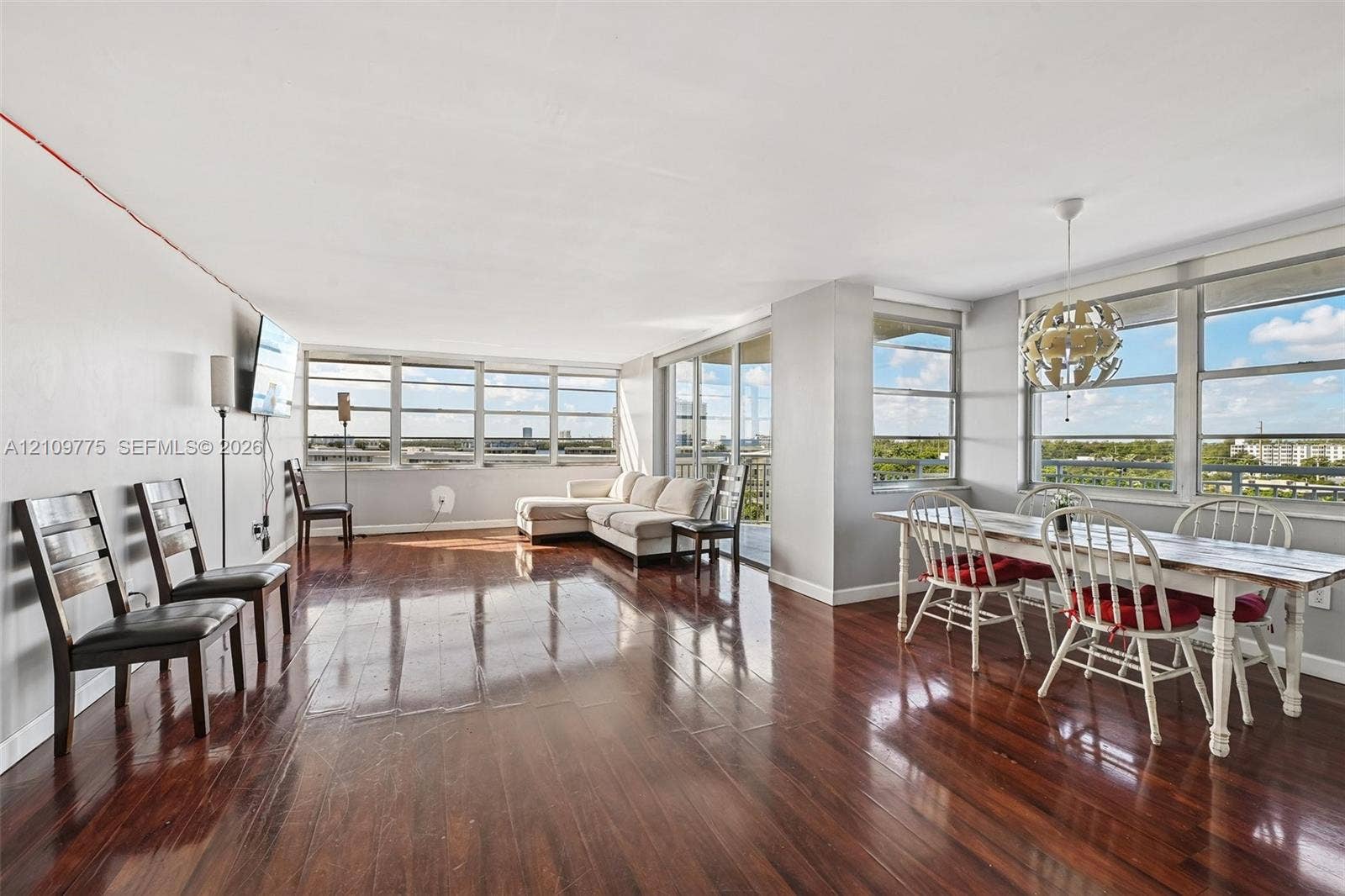 Expansive open-concept living area featuring polished wood-finish flooring, floor-to-ceiling windows, and a built-in overhead light fixture