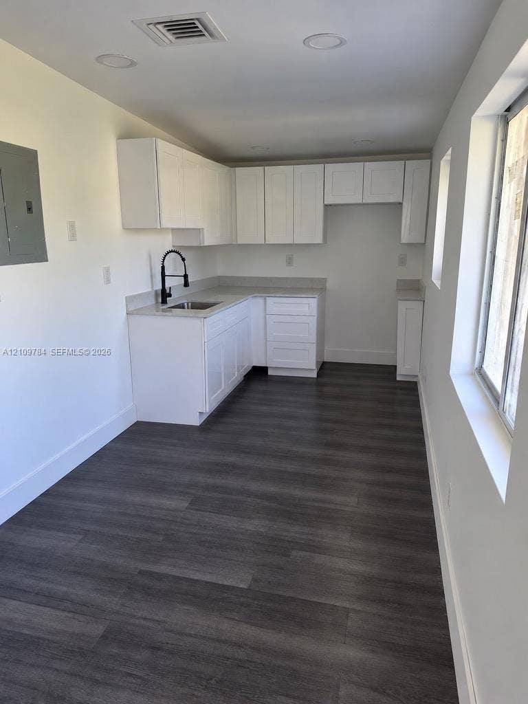 White shaker-style cabinetry, neutral stone-finish countertops, wood-finish flooring, recessed lighting, and a matte black gooseneck faucet