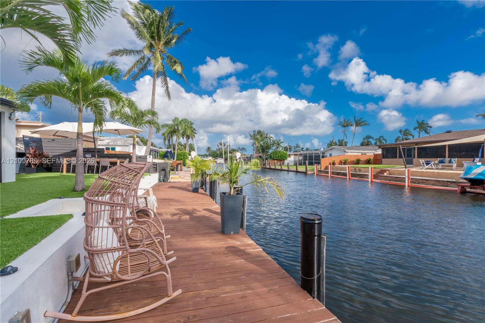 1469 NW 10th Street, #1471, Dania, Dania Beach, FL 33004 Waterfront property featuring a wooden deck, seawall, artificial turf area, and mature palm trees
