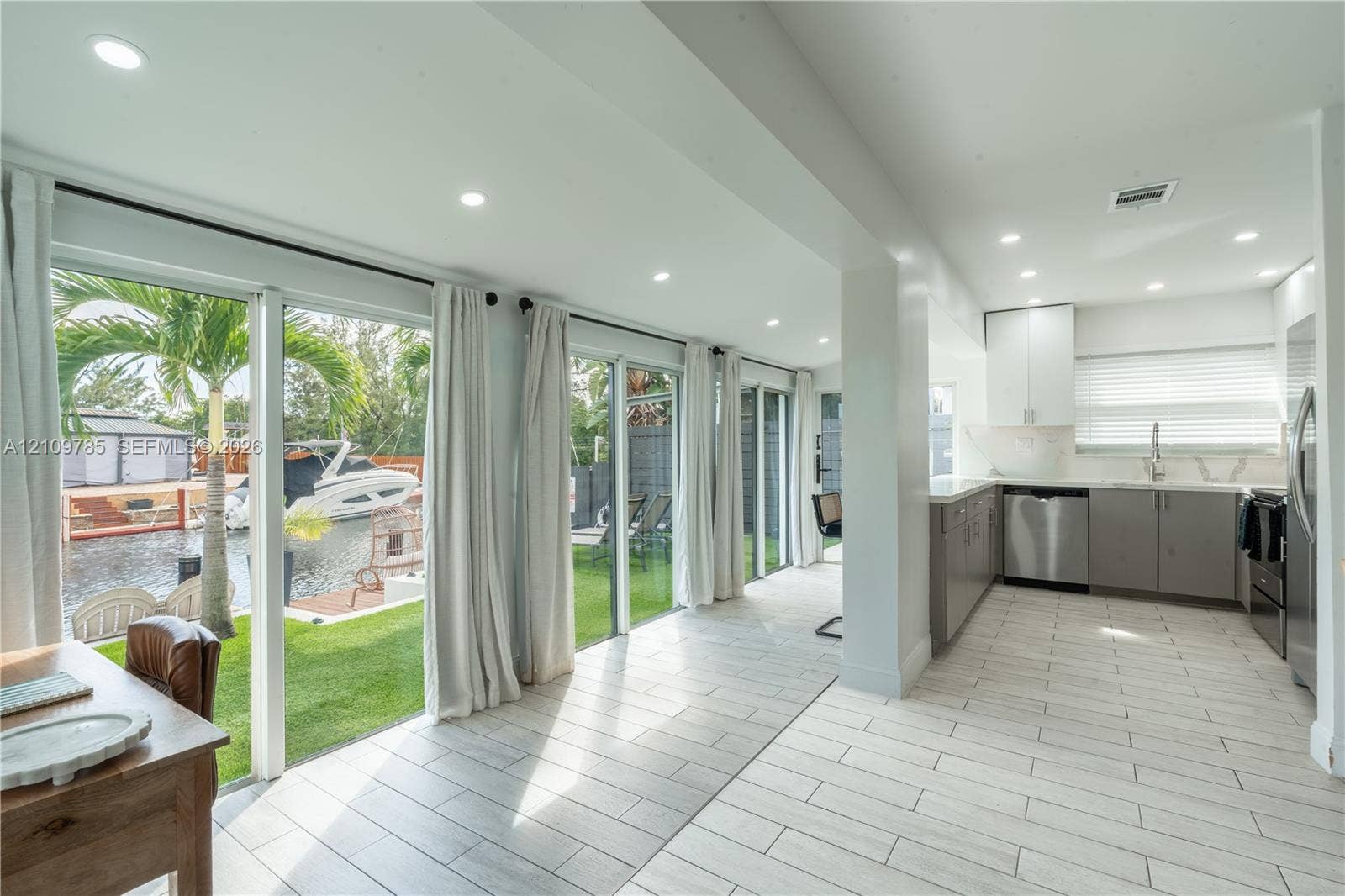 1469 NW 10th Street, #1471, Dania, Dania Beach, FL 33004 Kitchen featuring stainless steel appliances, white upper cabinetry, grey lower cabinetry, and recessed lighting, paired with floor-to-ceiling glass sliding doors opening to a waterfront lawn and boat dock
