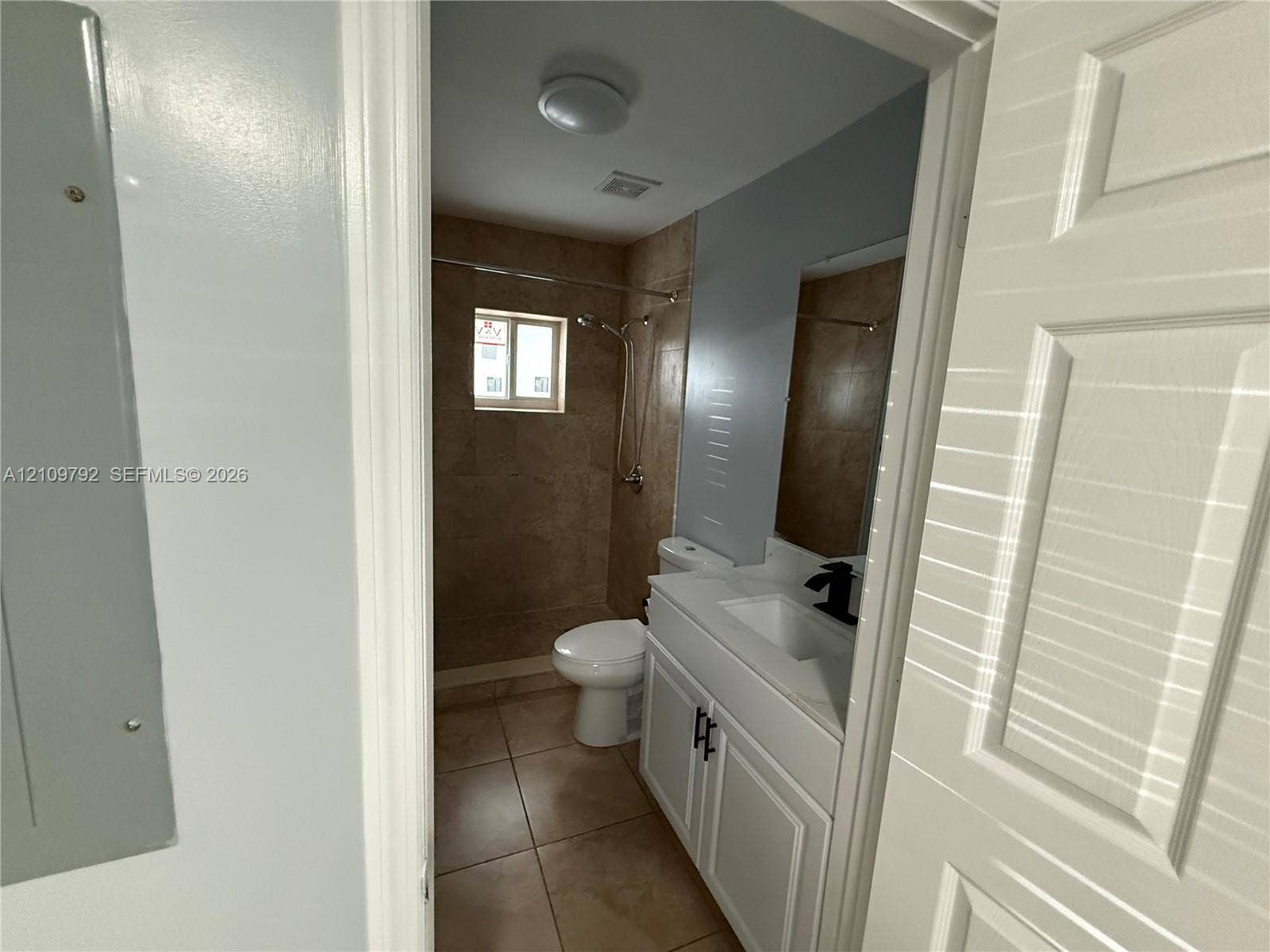 Bathroom featuring a white vanity cabinet with a rectangular vessel sink, matte black faucet, stone-finish floor tiling, and a tiled shower enclosure