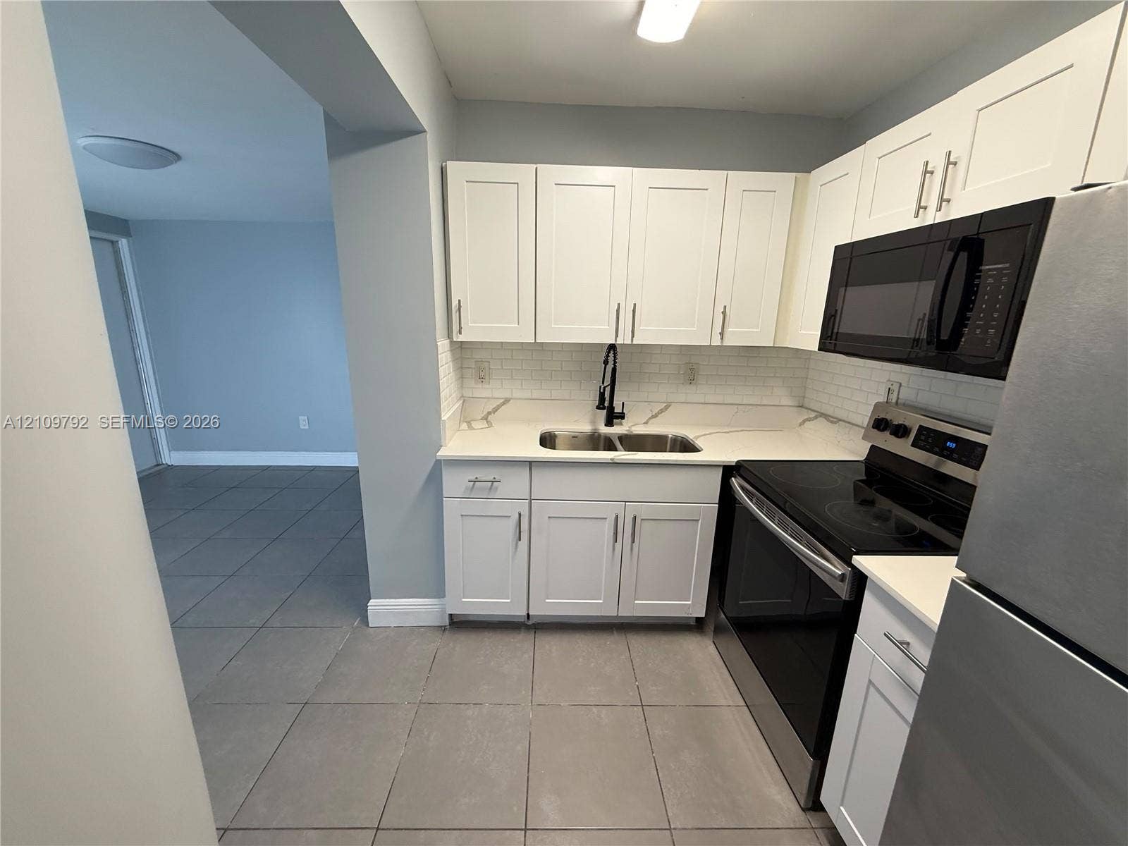 Kitchen featuring white shaker-style cabinetry, white countertops with grey veining, a white subway tile backsplash, a dual-basin stainless steel sink with a matte black faucet, and stainless steel appliances