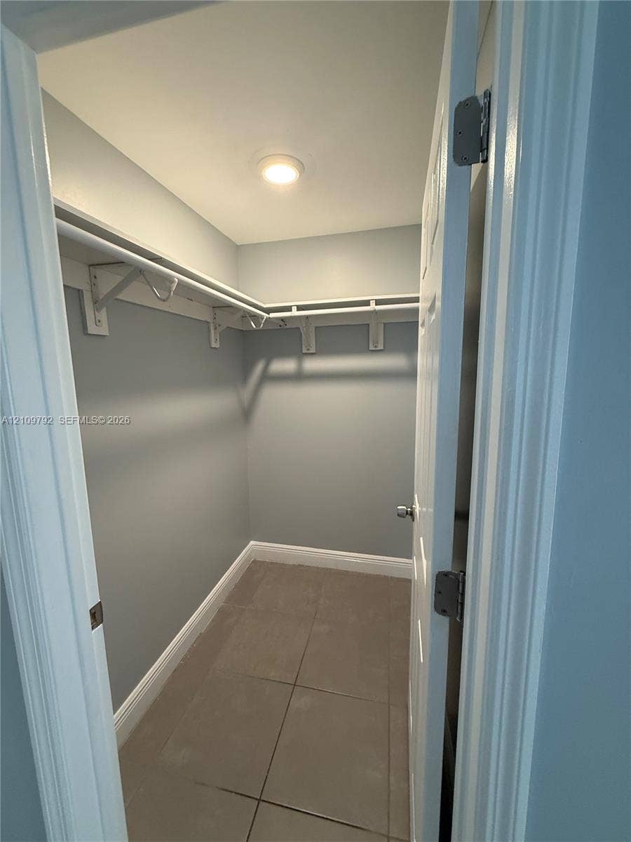 Walk-in closet featuring large-format tile flooring, built-in shelving, and overhead lighting