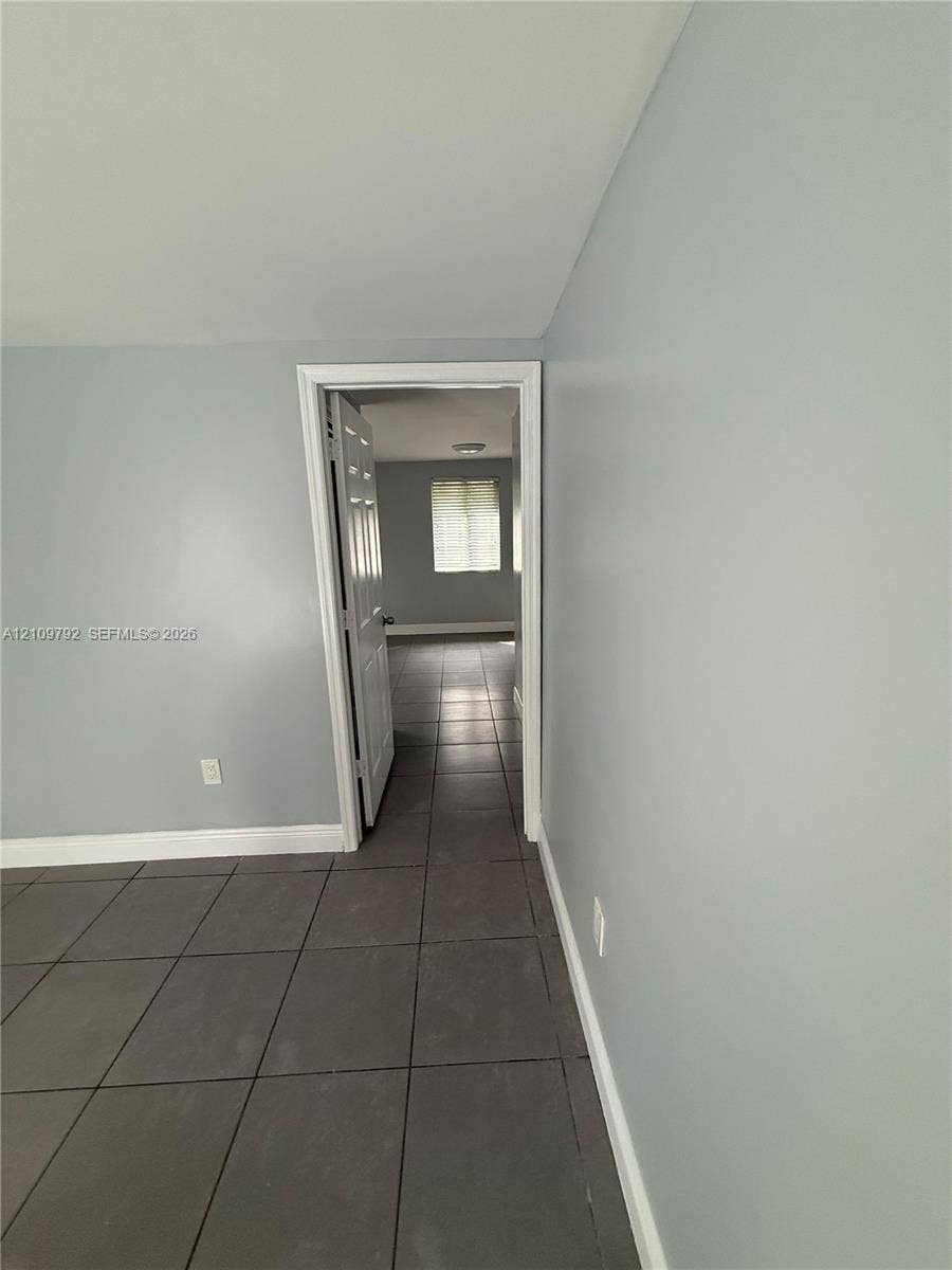 Neutral-toned interior featuring large-format ceramic tile flooring, a six-panel interior door, and a multi-pane window