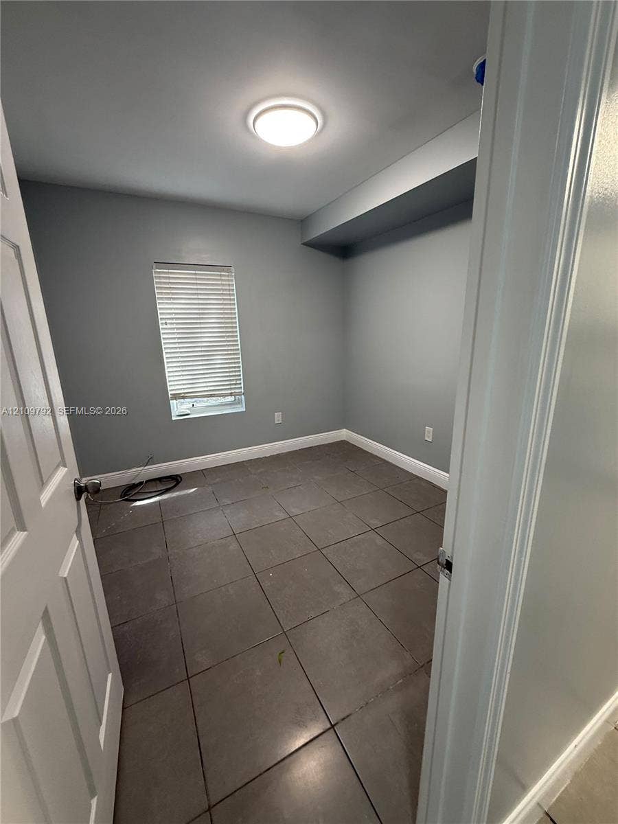 Room featuring large-format grey tile flooring, neutral wall paint, a flush-mount ceiling light fixture, and a window with horizontal blinds