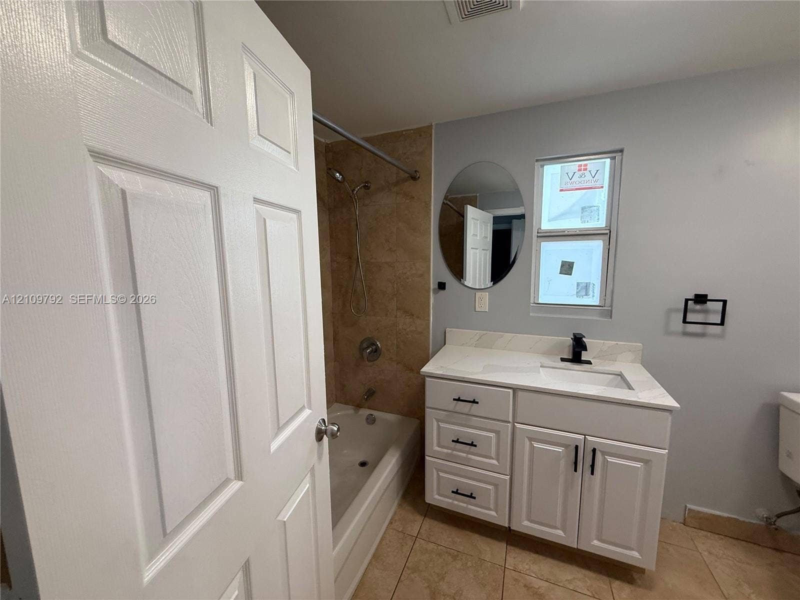 Bathroom featuring a white vanity with drawers and cabinet storage, a stone-surface countertop, a black faucet, a tub-shower combination with tiled surround, and an oval mirror
