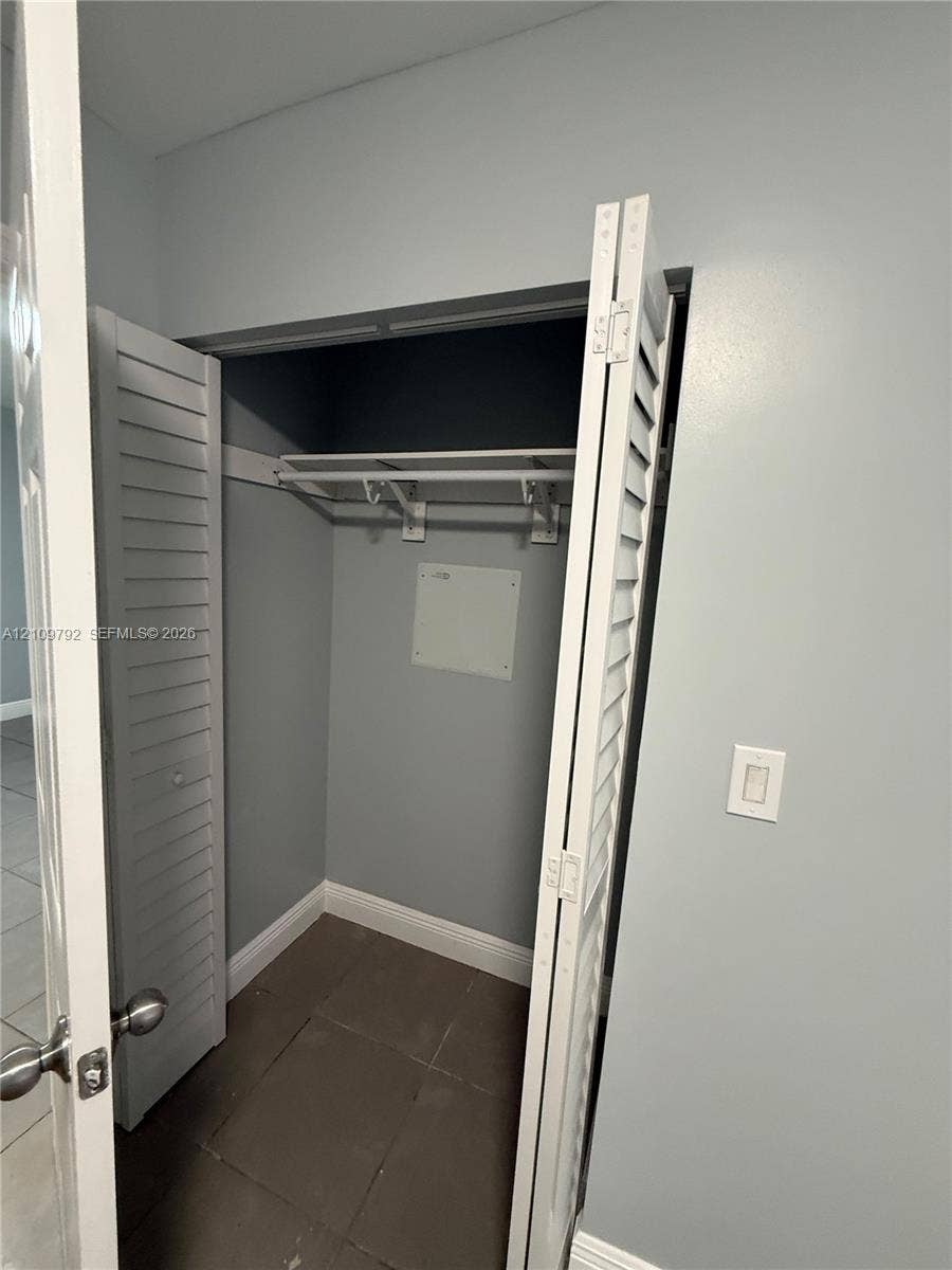 Closet featuring white louvered bifold doors, an integrated upper shelf with a hanging rod, and tile flooring