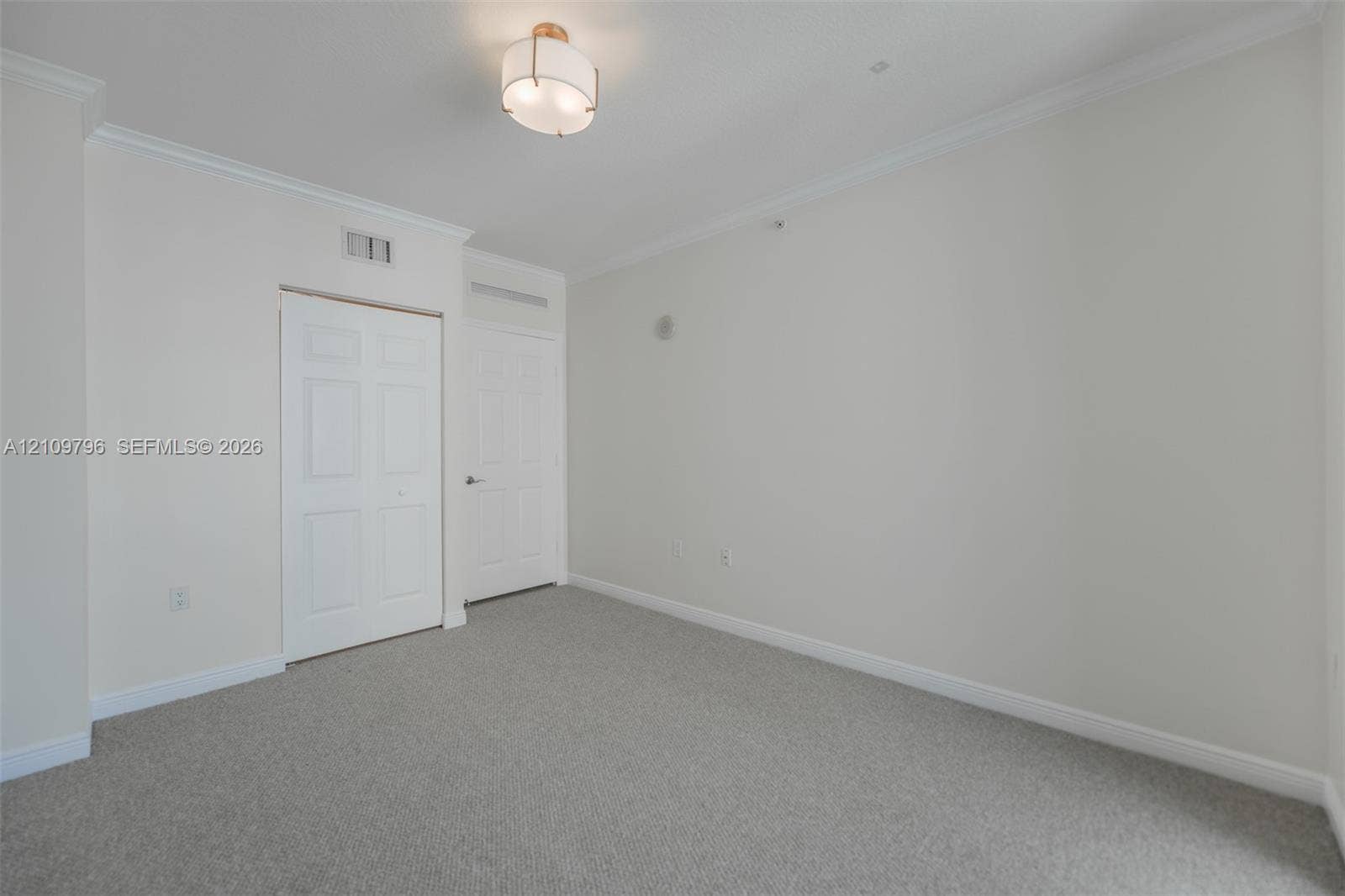 Interior space featuring neutral wall tones, crown molding, wall-to-wall carpeting, a semi-flush mount light fixture, and a multi-panel closet door