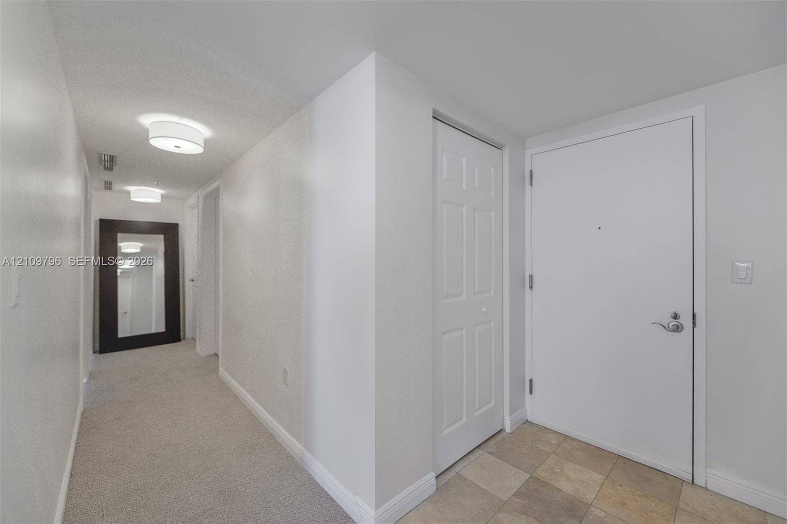 Entryway featuring neutral-toned floor tiling, wall-to-wall carpeting, and dual ceiling-mounted drum light fixtures