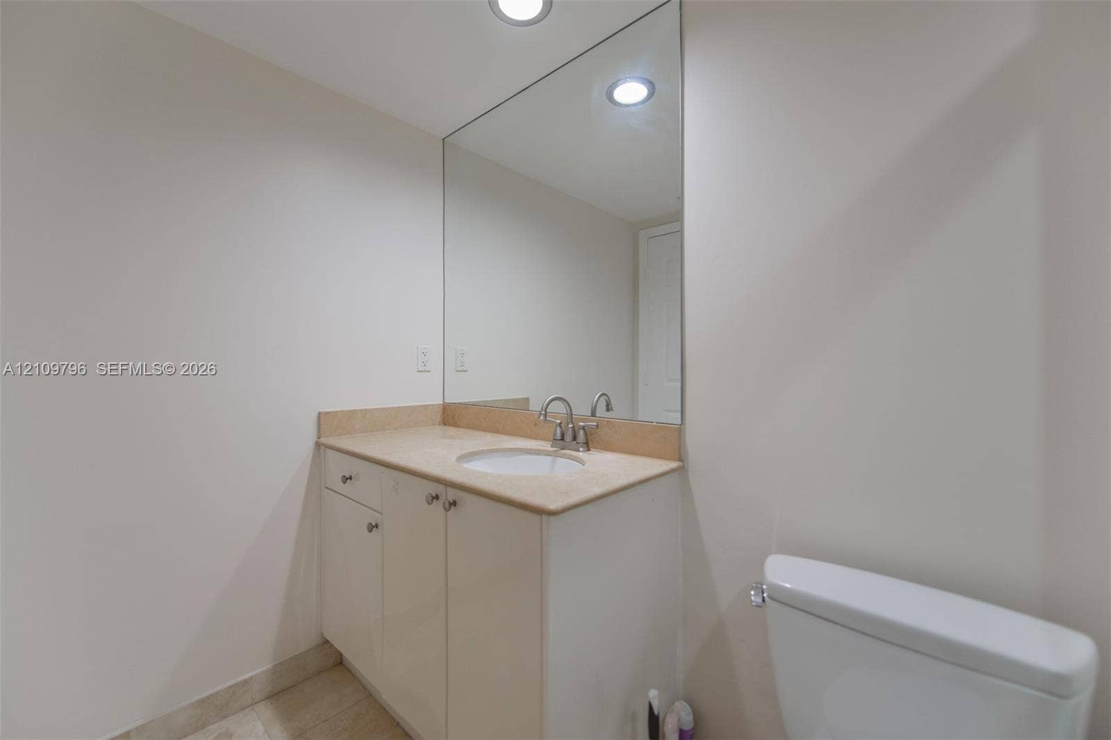 Bathroom vanity featuring a stone-surface countertop, an integrated undermount sink, brushed-metal hardware, a large frameless wall-mounted mirror, and recessed ceiling lighting