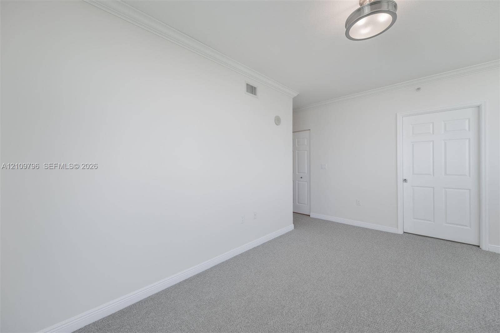 Neutral-toned interior space featuring wall-to-wall carpeting, crown molding, a semi-flush mount ceiling light fixture, and six-panel interior doors