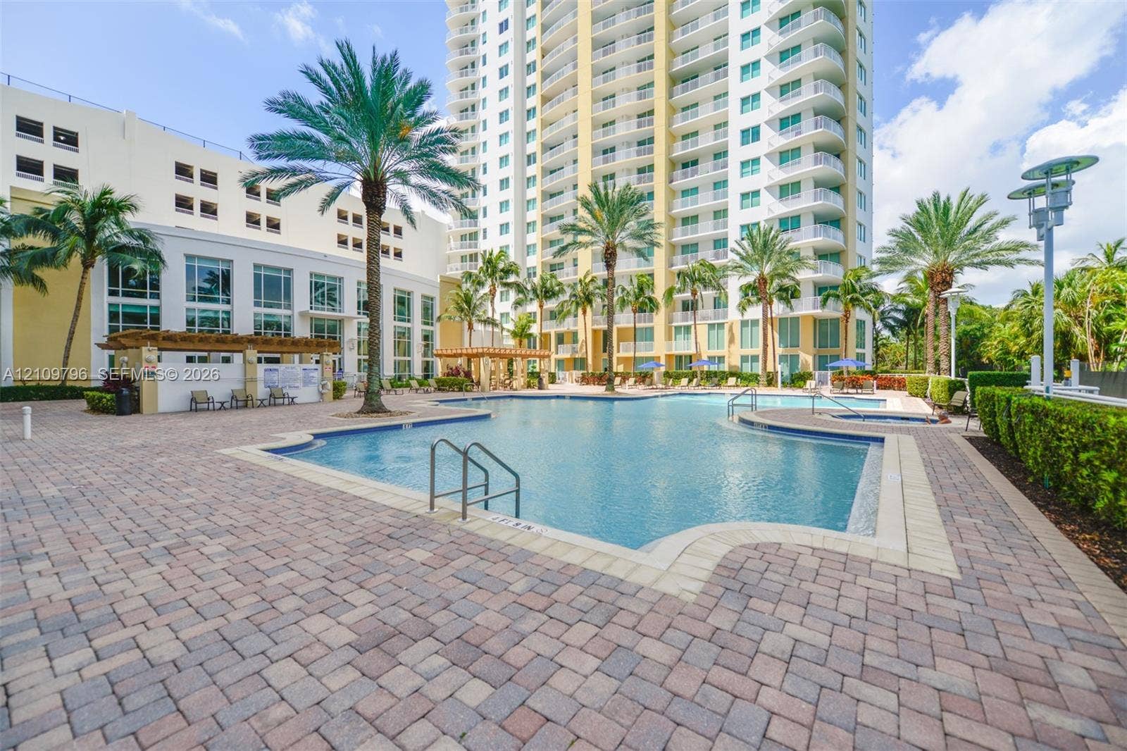 Swimming pool with tile surround, paver decking, attached spa, wooden pergola, and mature palm trees