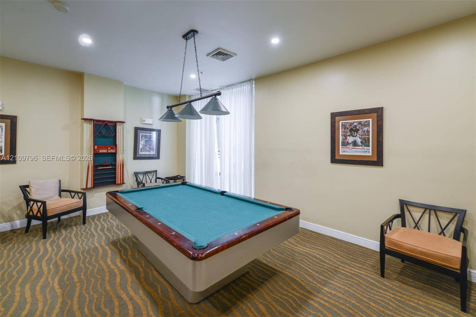 Interior room featuring patterned wall-to-wall carpeting, recessed ceiling lighting, a three-light pendant fixture, and floor-to-ceiling sheer window treatments