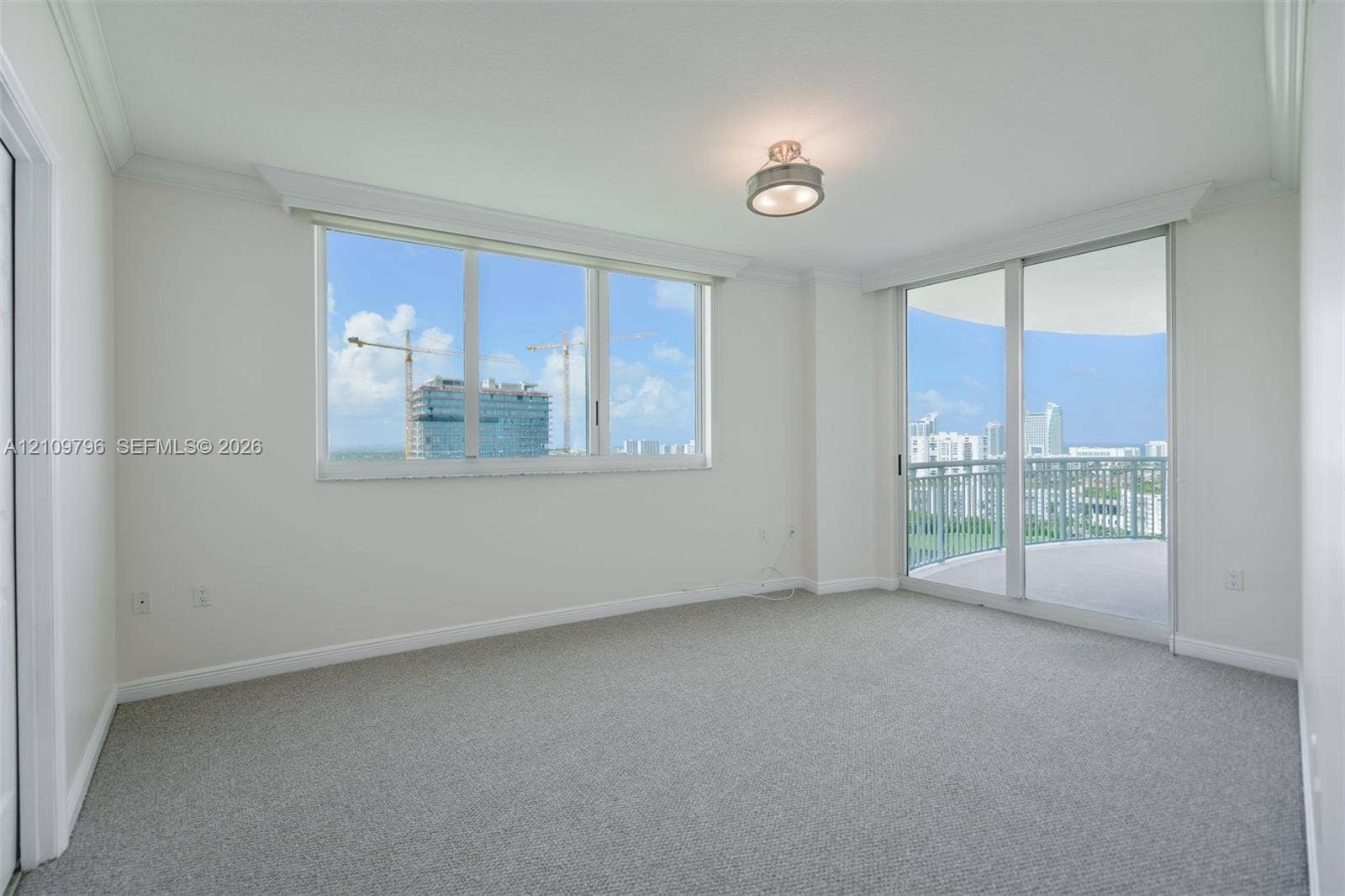 Bright interior space featuring expansive windows, glass sliding doors, neutral carpeting, crown molding, and a private balcony