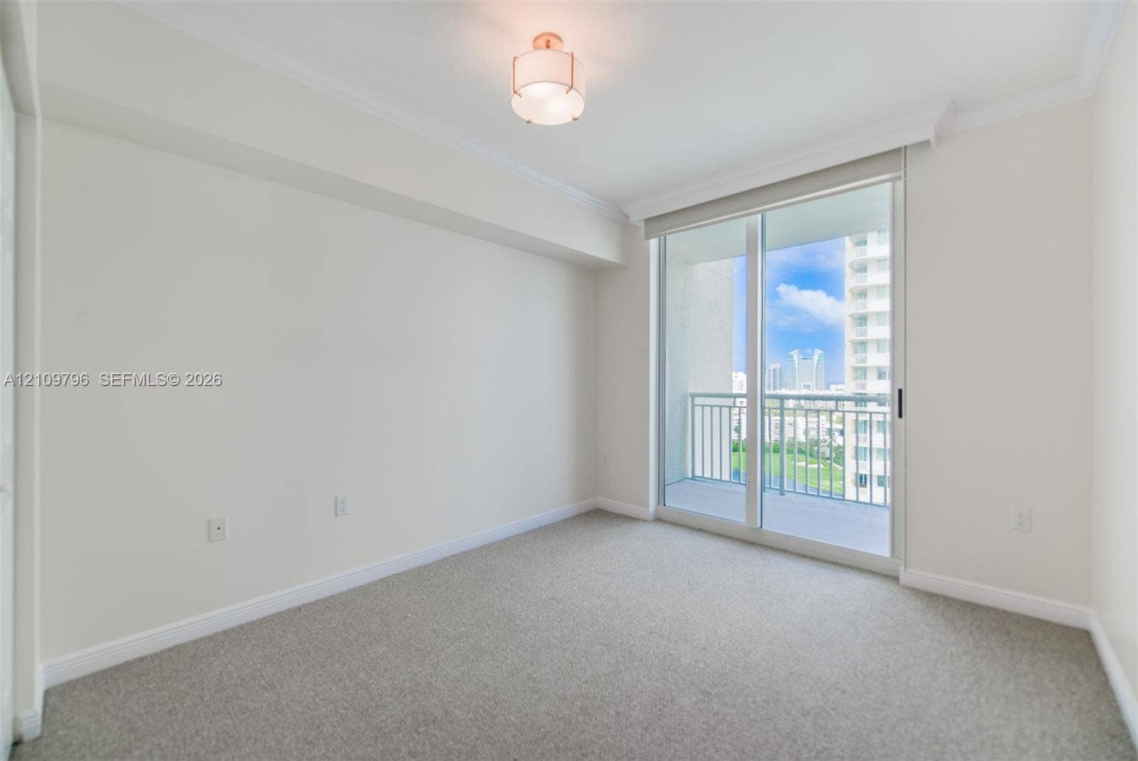 Neutral-toned wall-to-wall carpeting, crown molding, drum-style ceiling light fixture, and sliding glass door with access to a balcony