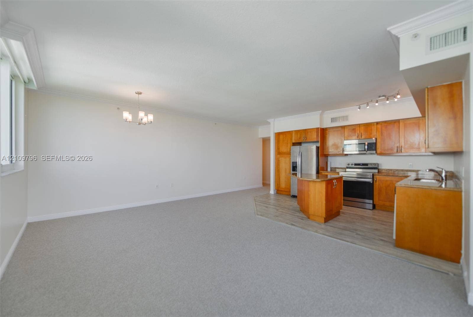 Open-concept space featuring wood-finish cabinetry, stainless steel appliances, a kitchen island, and crown molding