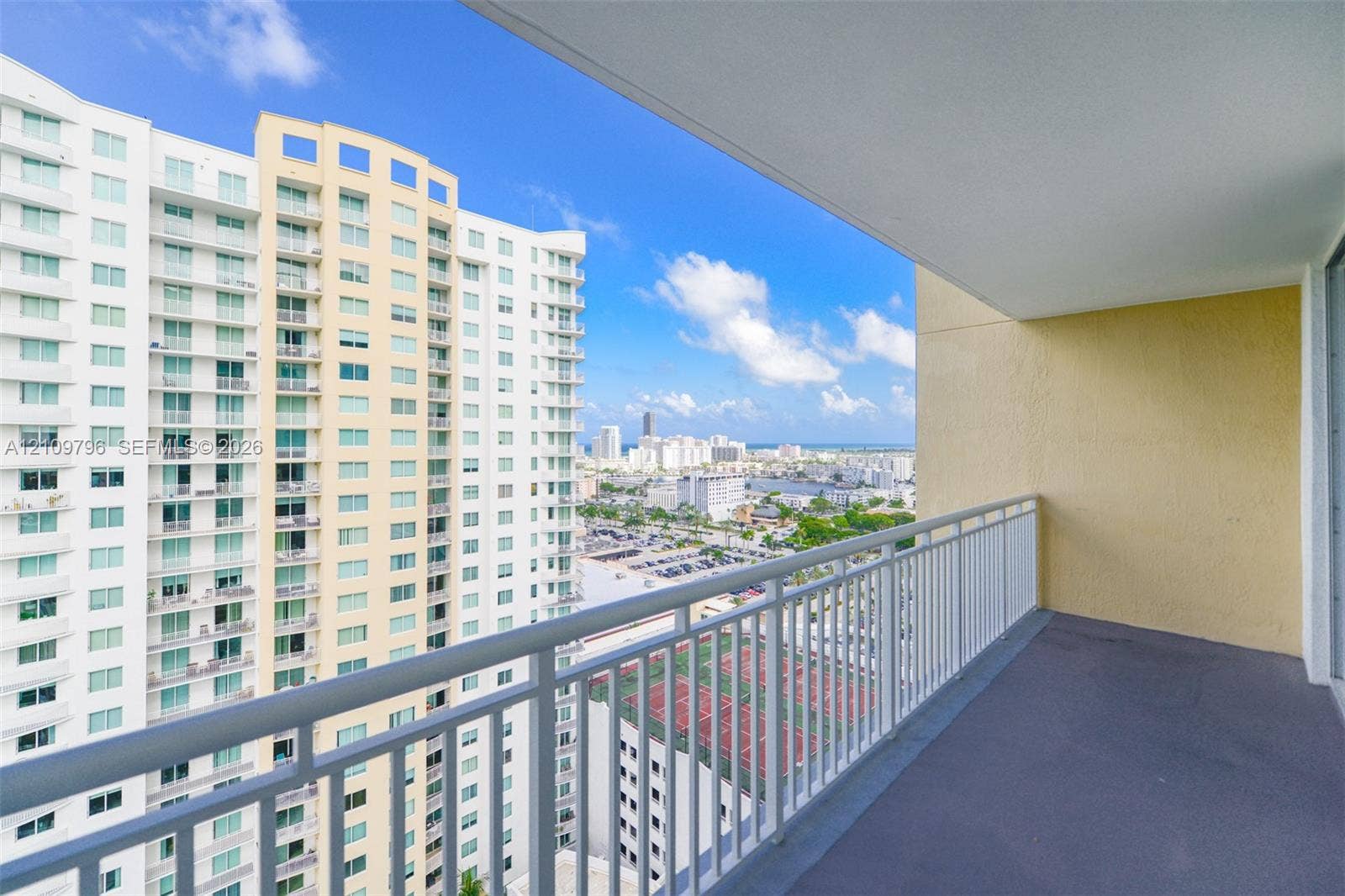 Covered balcony featuring a white metal railing, concrete flooring, and an expansive urban backdrop