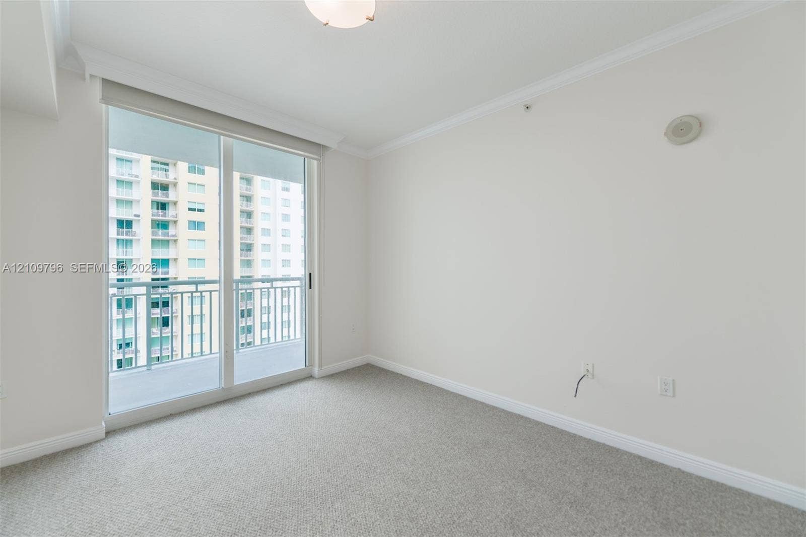 Neutral-toned interior featuring wall-to-wall carpeting, crown molding, and a sliding glass door providing access to a private balcony