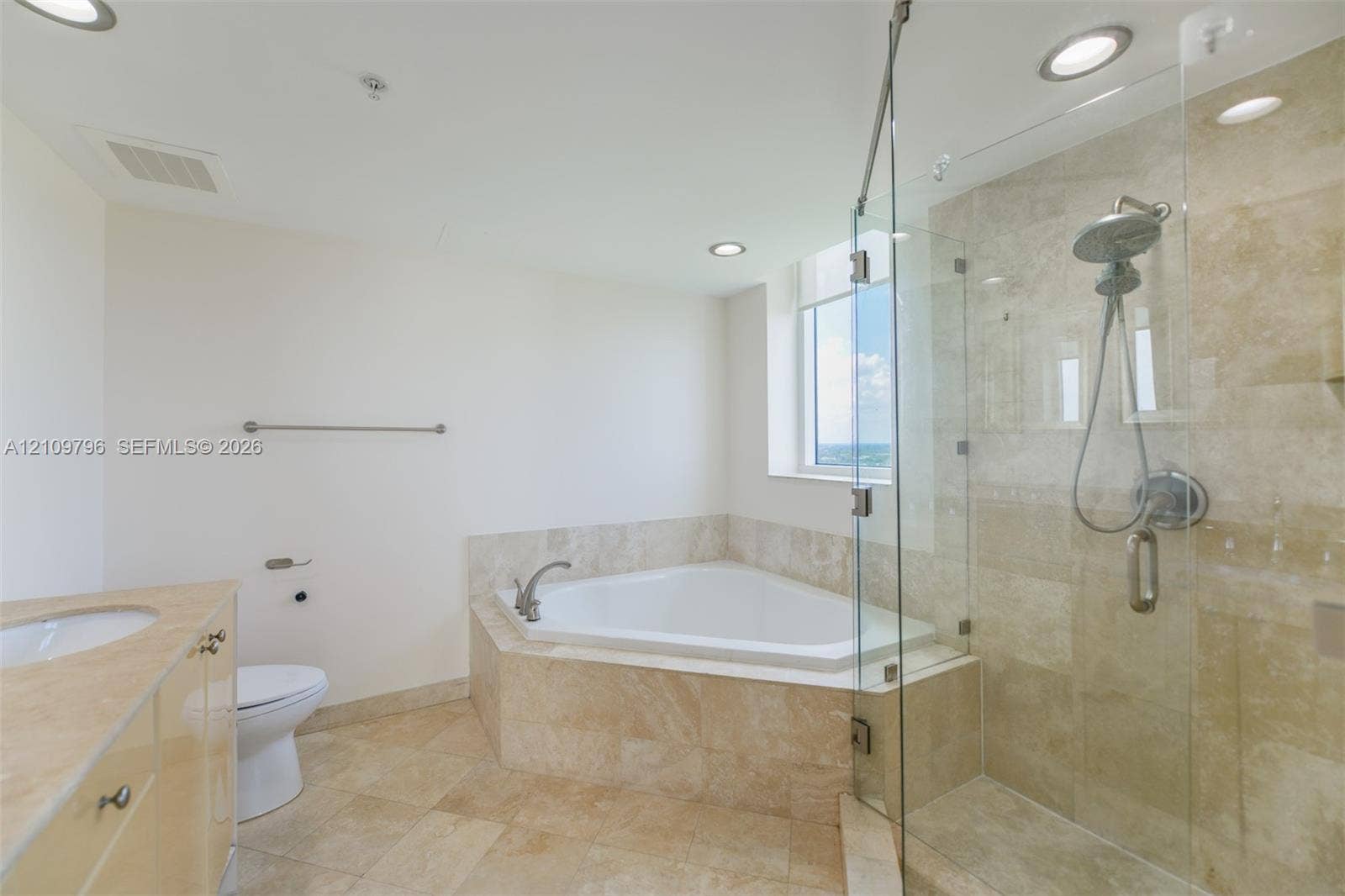 Corner soaking tub with natural stone surround, glass-enclosed shower with stone tile, stone-topped vanity, and recessed lighting