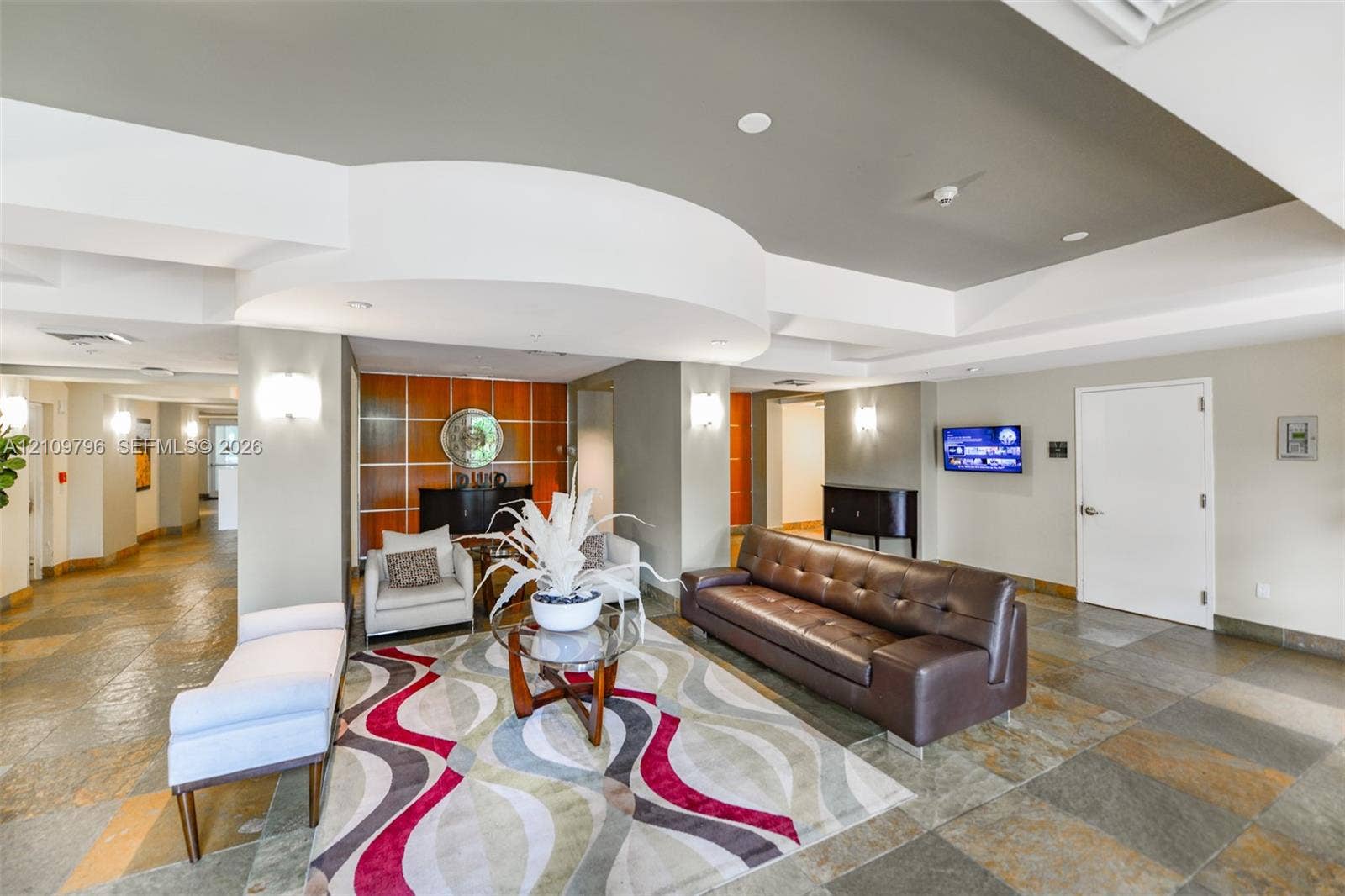 Grand lobby featuring multi-toned stone flooring, a tiered tray ceiling with recessed lighting, and decorative wall paneling