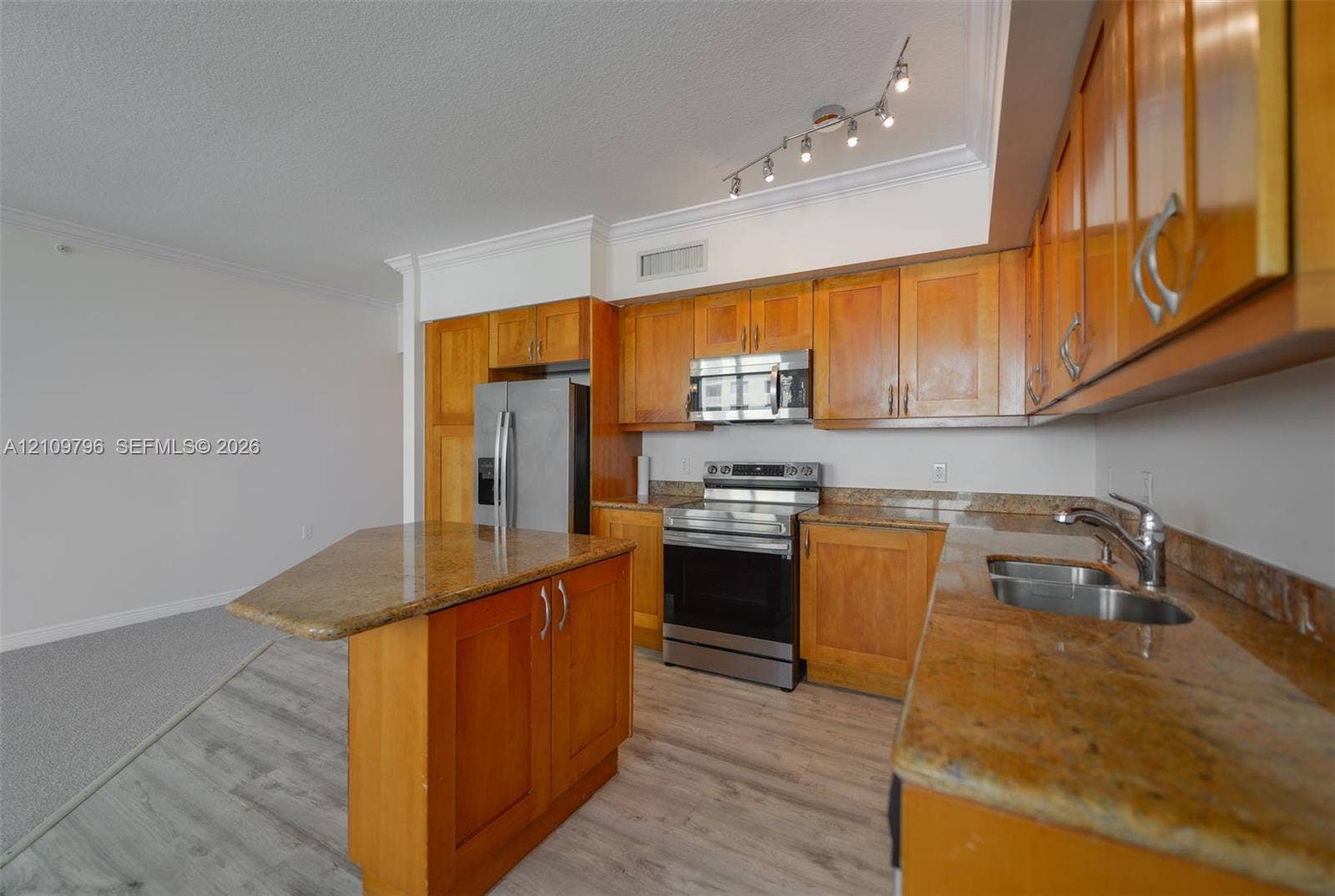 Kitchen featuring wood cabinetry, stone countertops, stainless steel appliances, a center island, and track lighting