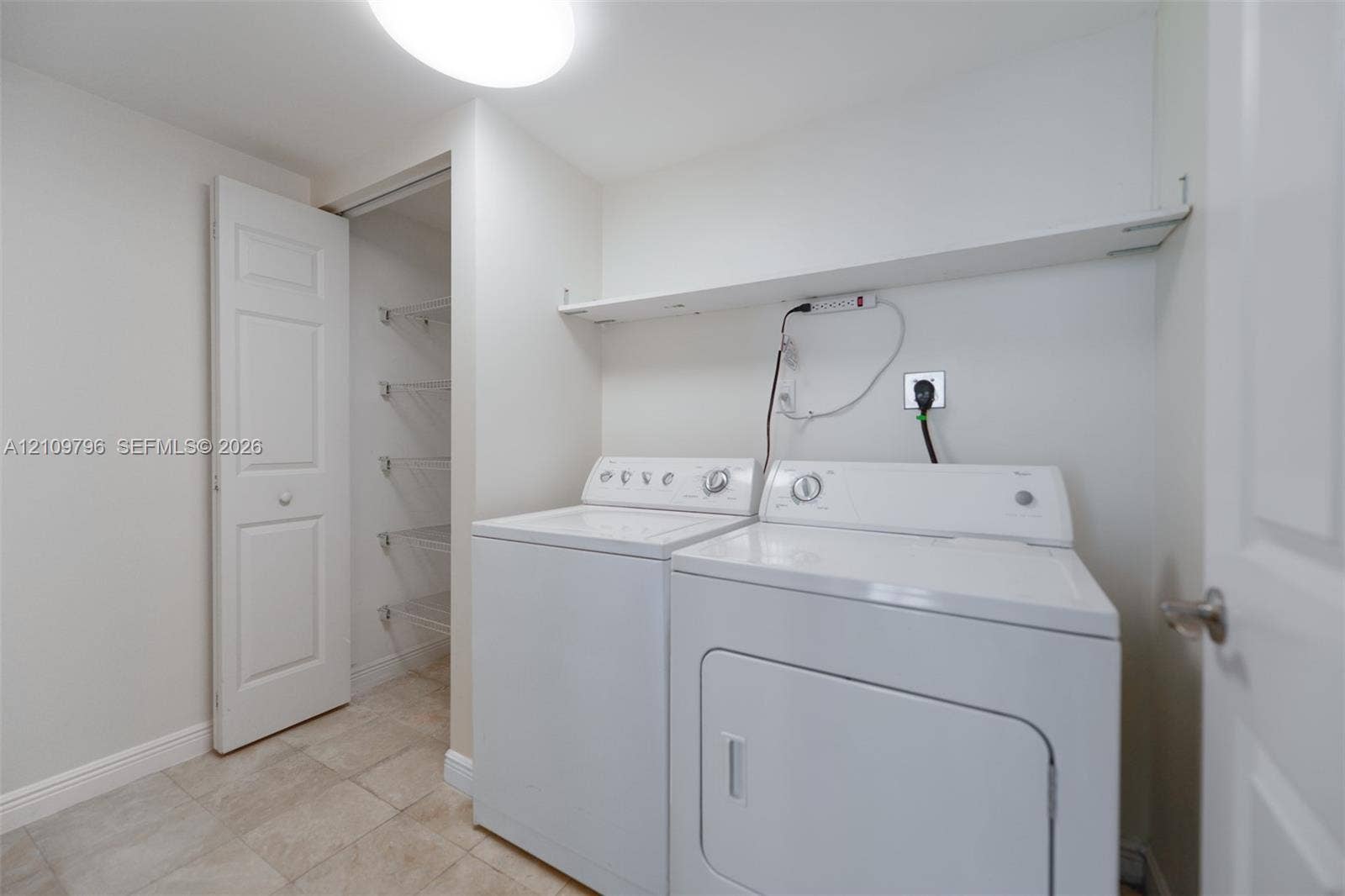 Laundry space featuring tile flooring, built-in wire shelving, and an overhead storage ledge