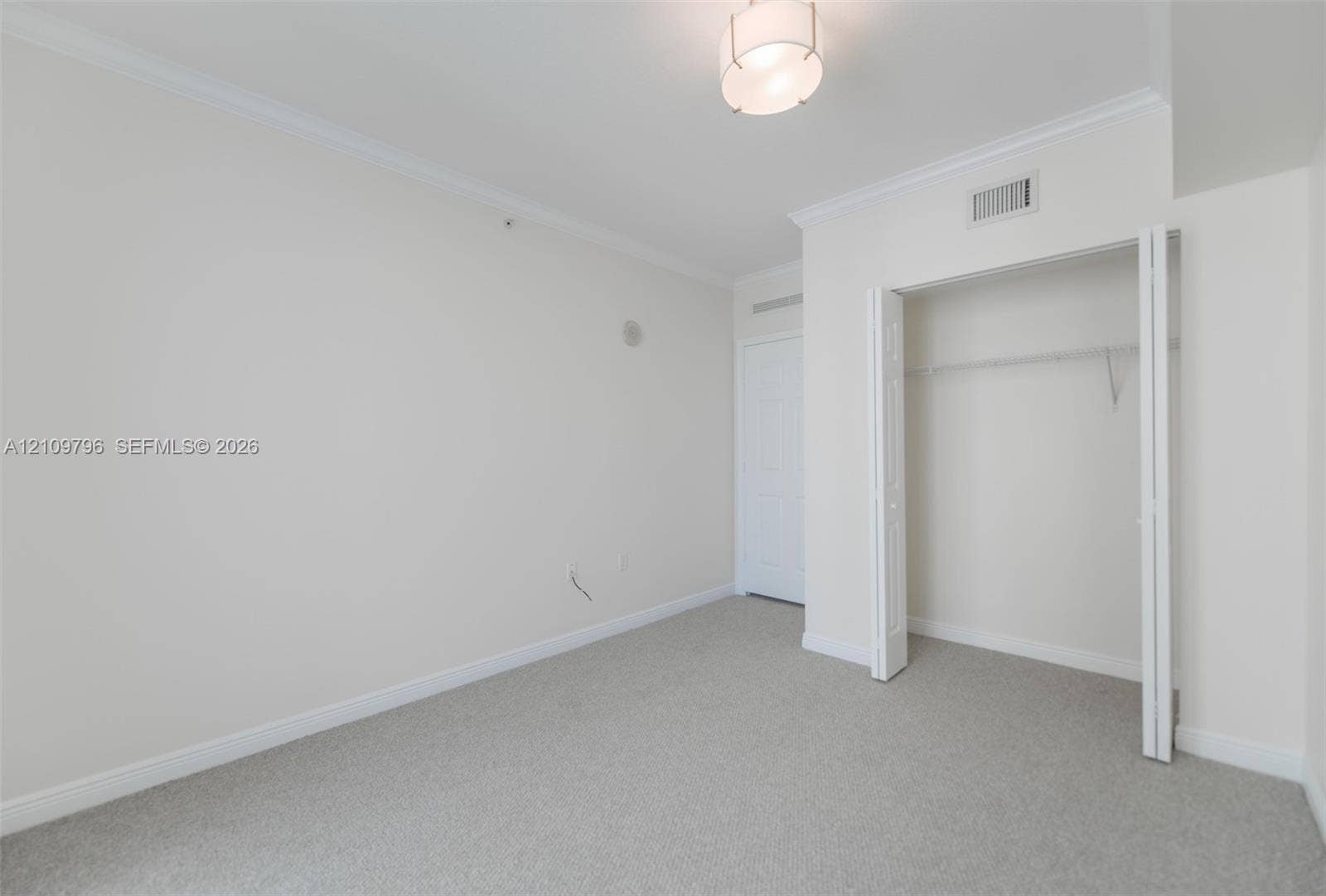 Neutral-toned wall-to-wall carpeting, crown molding, a semi-flush mount drum light fixture, and a closet with bifold doors