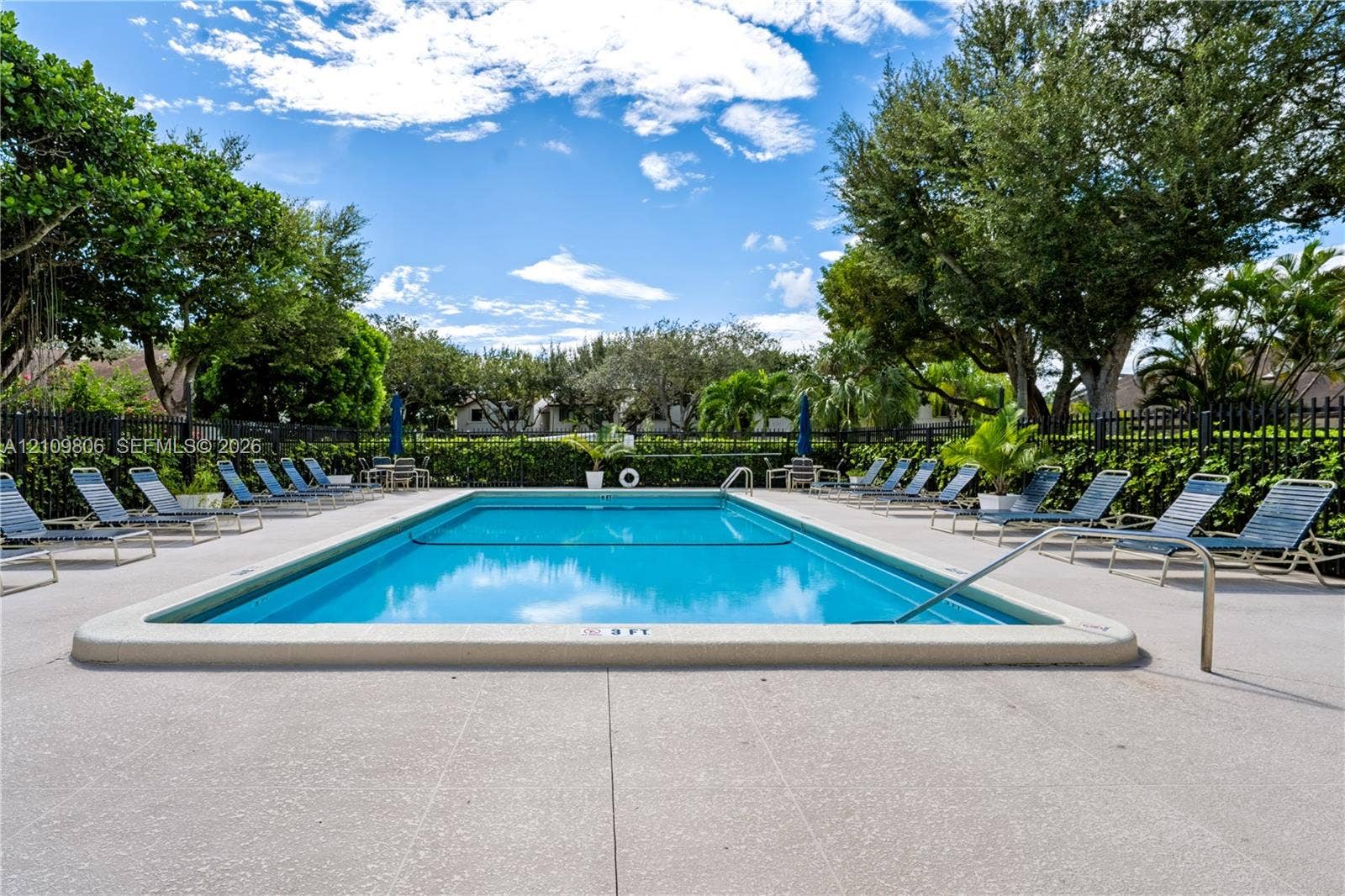 9123 SW 117th Court, Miami, FL 33186 Rectangular swimming pool featuring a concrete deck and perimeter black metal fencing surrounded by mature landscaping