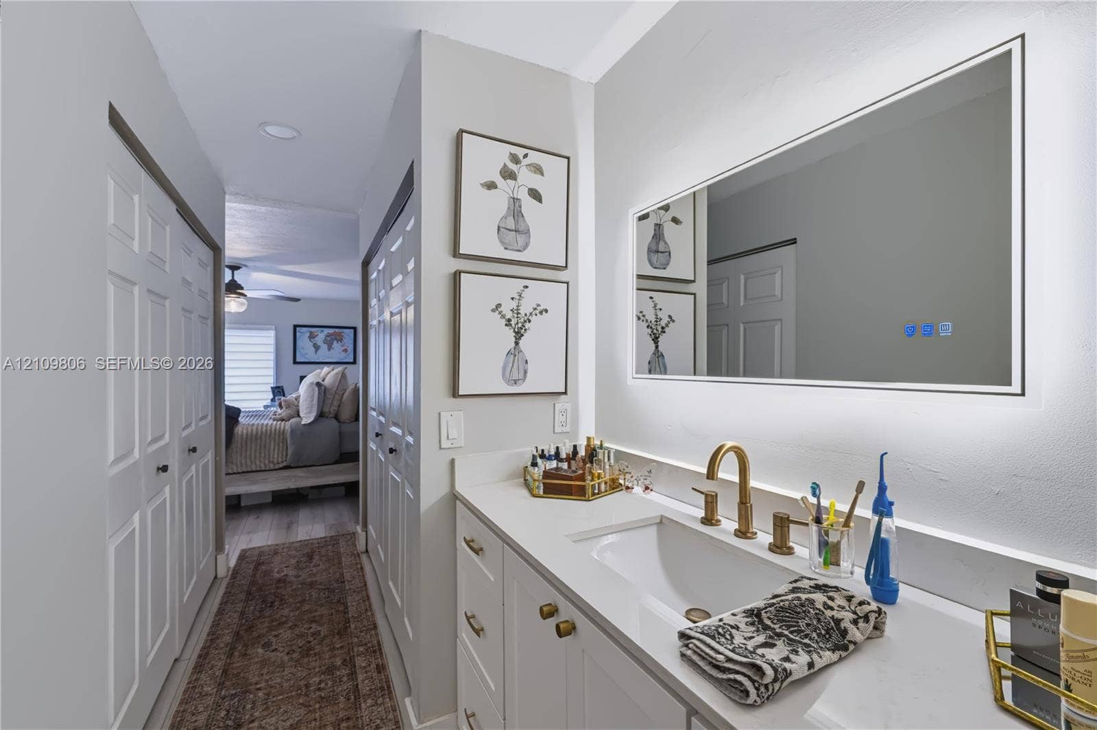 9123 SW 117th Court, Miami, FL 33186 Bathroom vanity featuring white cabinetry, a solid surface countertop with an integrated basin, a gold-tone widespread faucet, and a large rectangular LED-backlit mirror