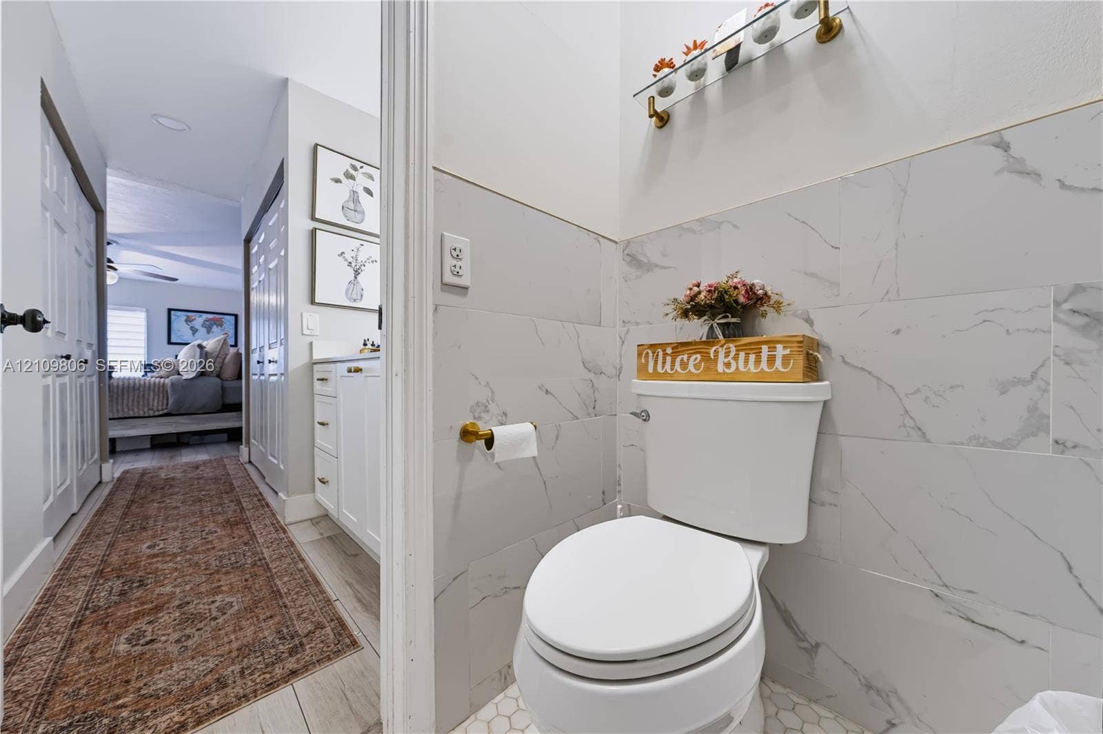 9123 SW 117th Court, Miami, FL 33186 Half-bath featuring large-format white stone-finish wall tile, brass-finish hardware, hexagonal floor tile, and a glass-shelf vanity fixture