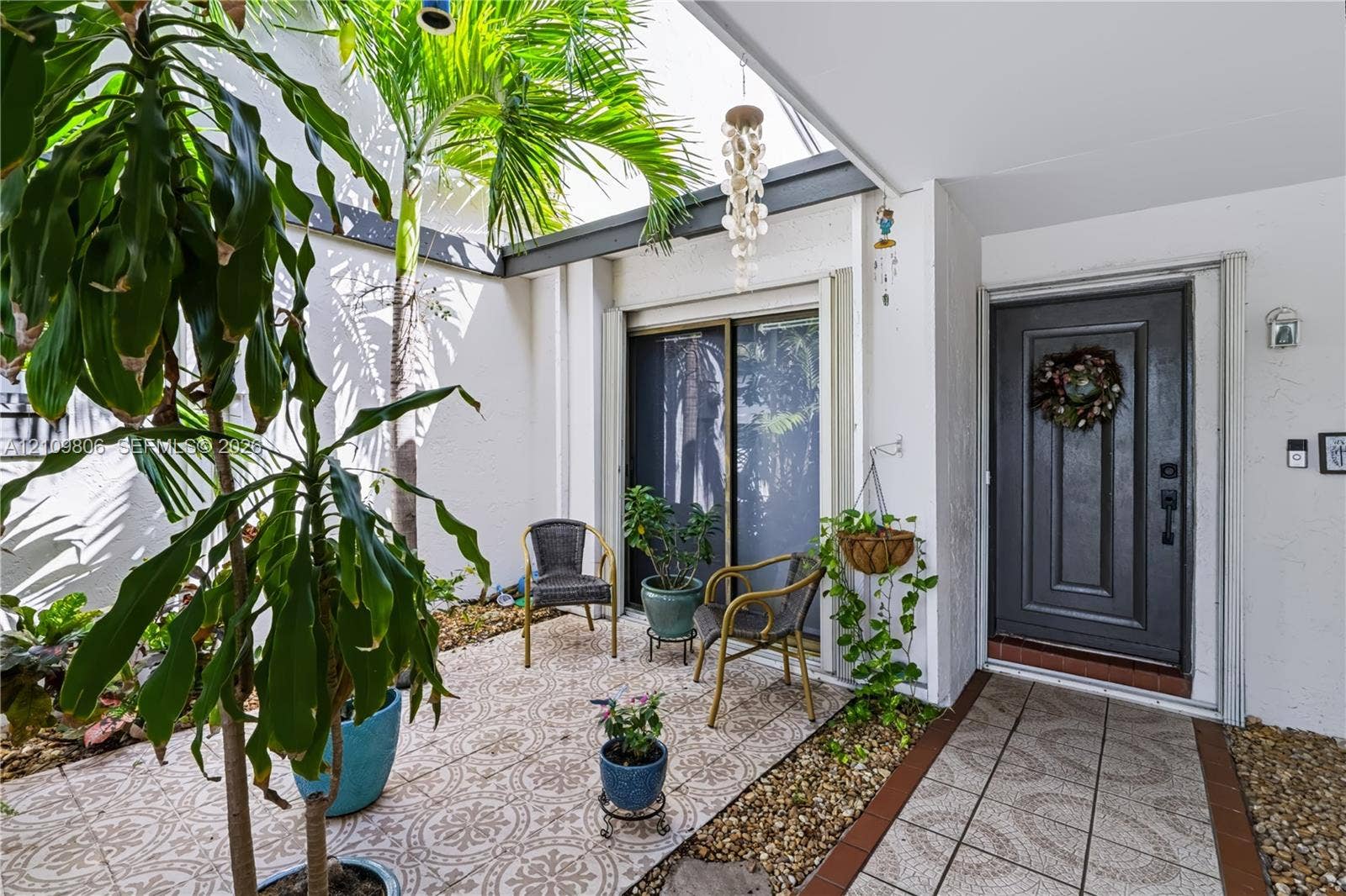 9123 SW 117th Court, Miami, FL 33186 Enclosed courtyard featuring patterned tile flooring, exposed structural beams, gravel landscaping, and a solid-panel front entry door